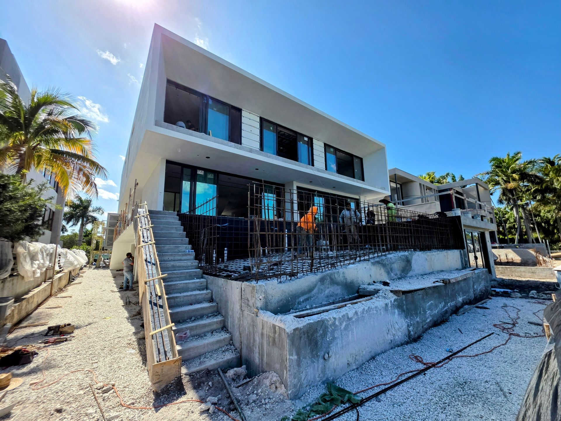 Modern white building with black framed windows, outdoor stairs, and construction debris. Sunny day.