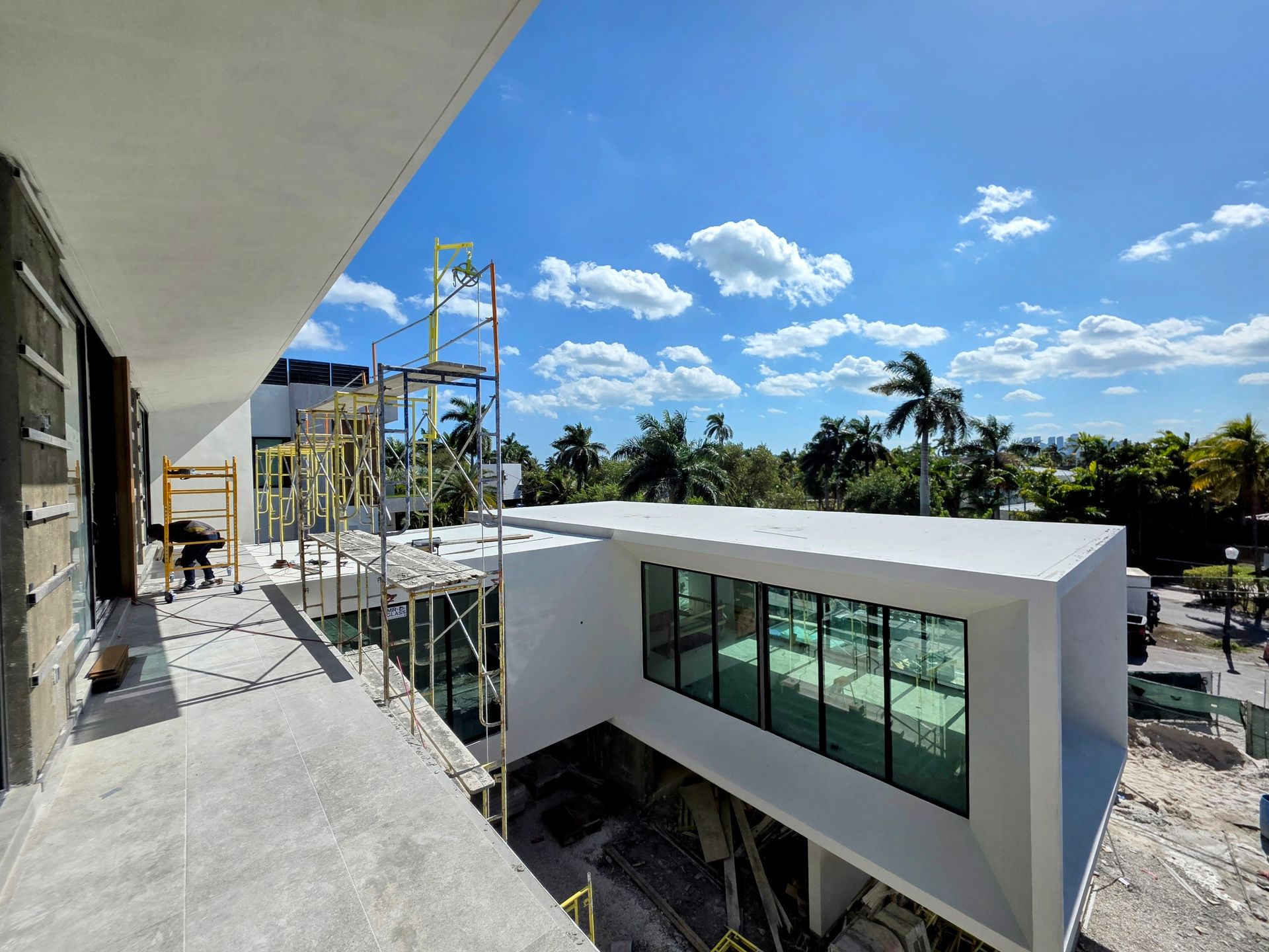 Exterior view of a modern building under construction with a bright blue sky and trees in the background.