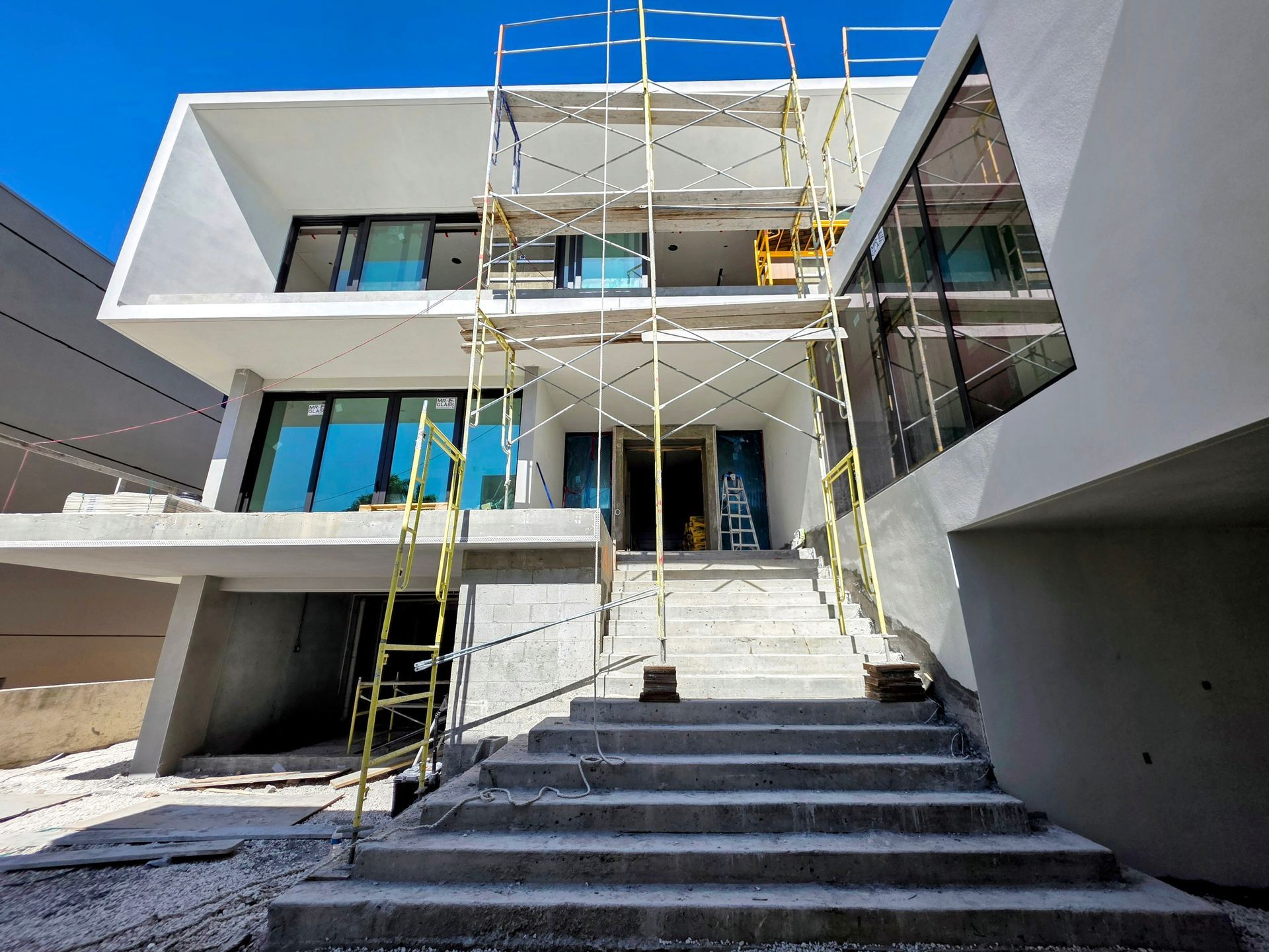 Exterior of a modern two-story building under construction, with scaffolding and concrete steps leading to the entrance.