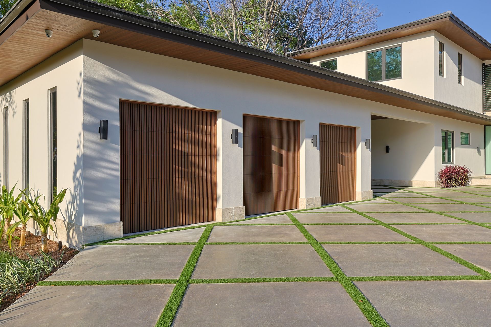 Beige stucco house with three wood garage doors and a patterned concrete driveway.