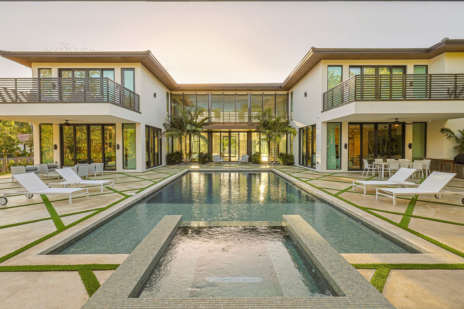 Luxury home with pool and patio furniture. White exterior, glass doors, and wooden balconies.