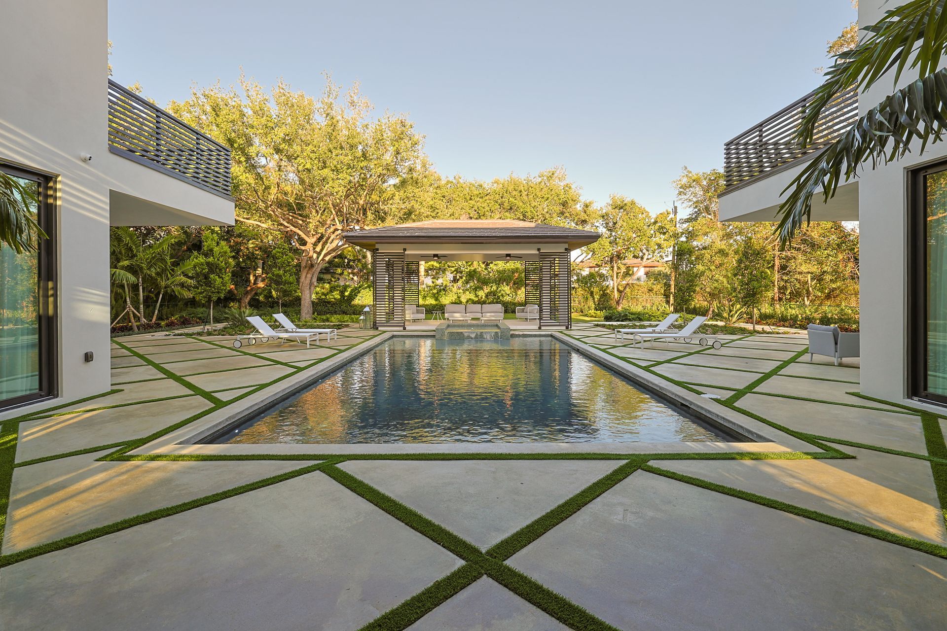 Luxurious pool area with patio, gazebo, and flanking white buildings. Blue water reflects sky.