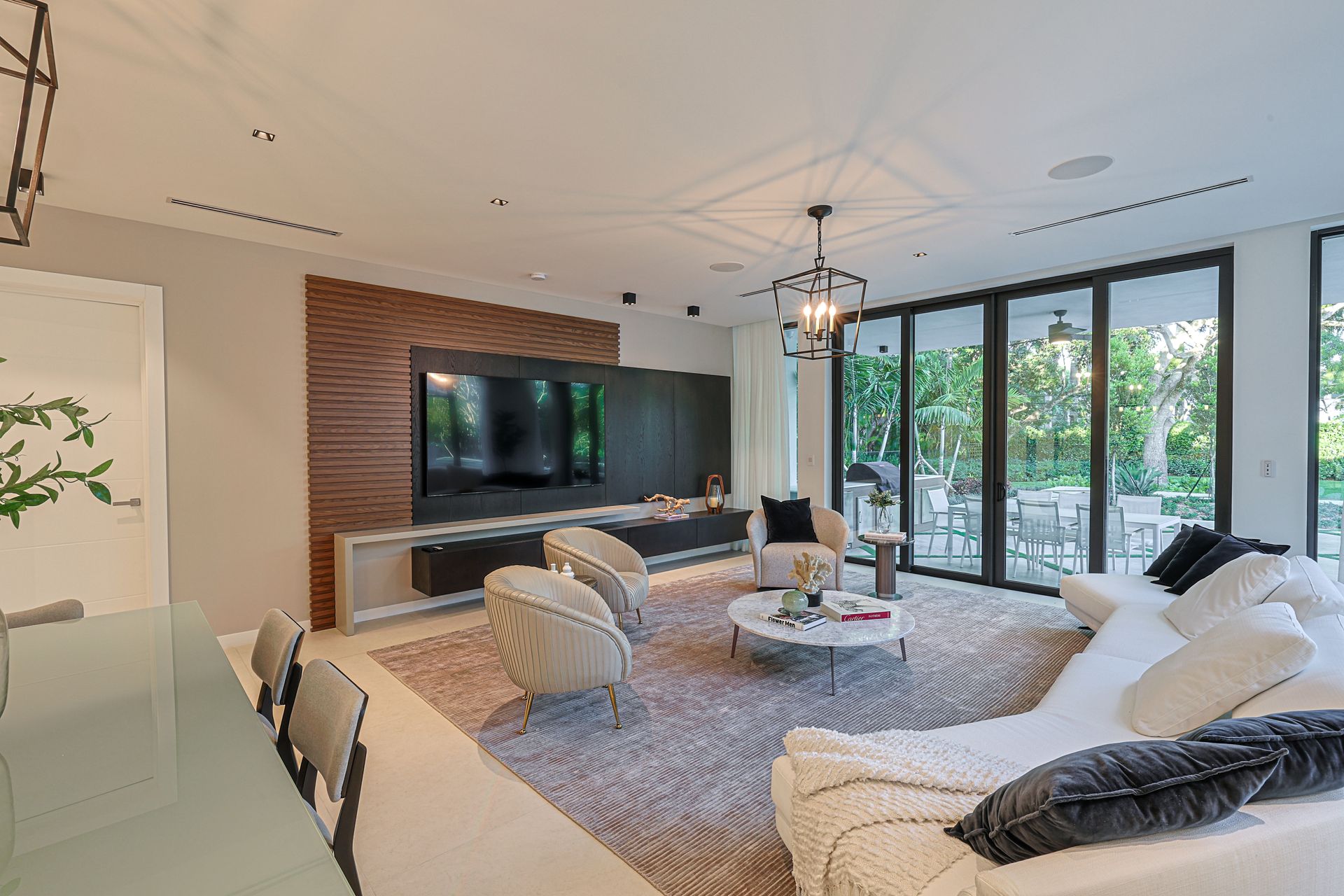 Modern living room with TV, sectional sofa, and floor-to-ceiling windows overlooking a patio.