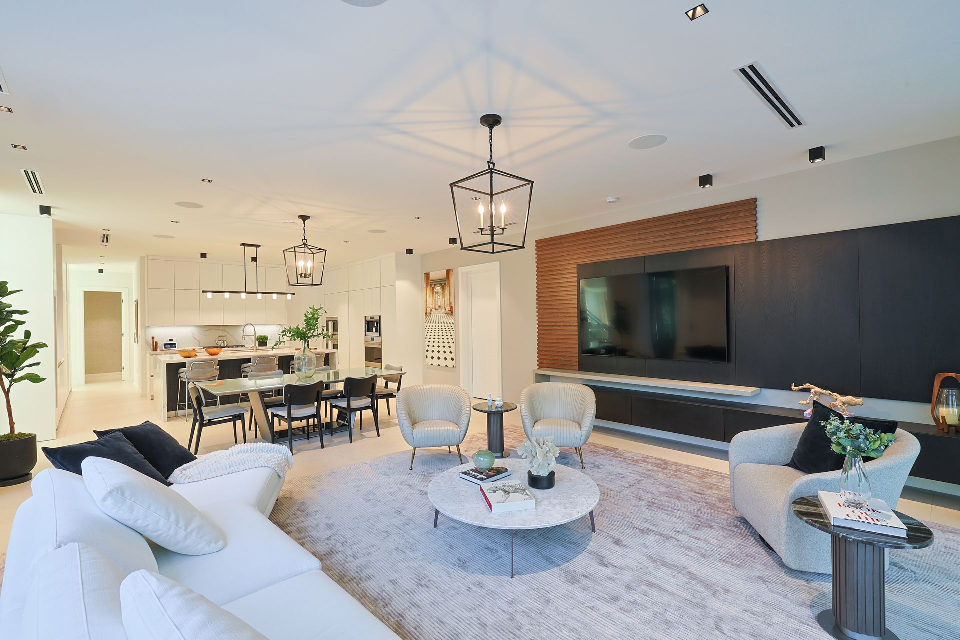 Open-plan living space with white sofa, armchairs, dining table, and dark accent wall with TV.