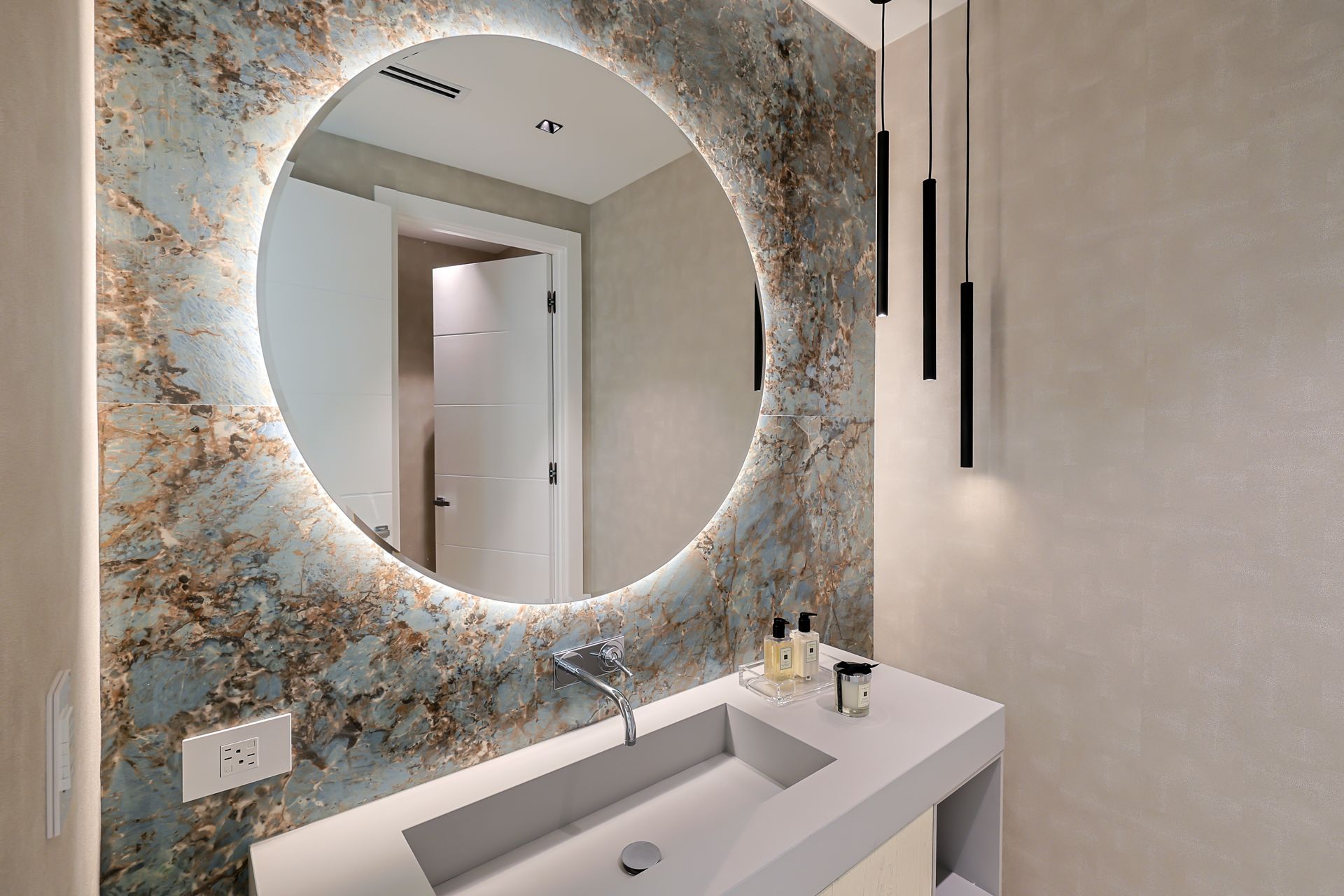 Modern bathroom with a round mirror and a sink. The wall behind the mirror is decorated with an abstract pattern.