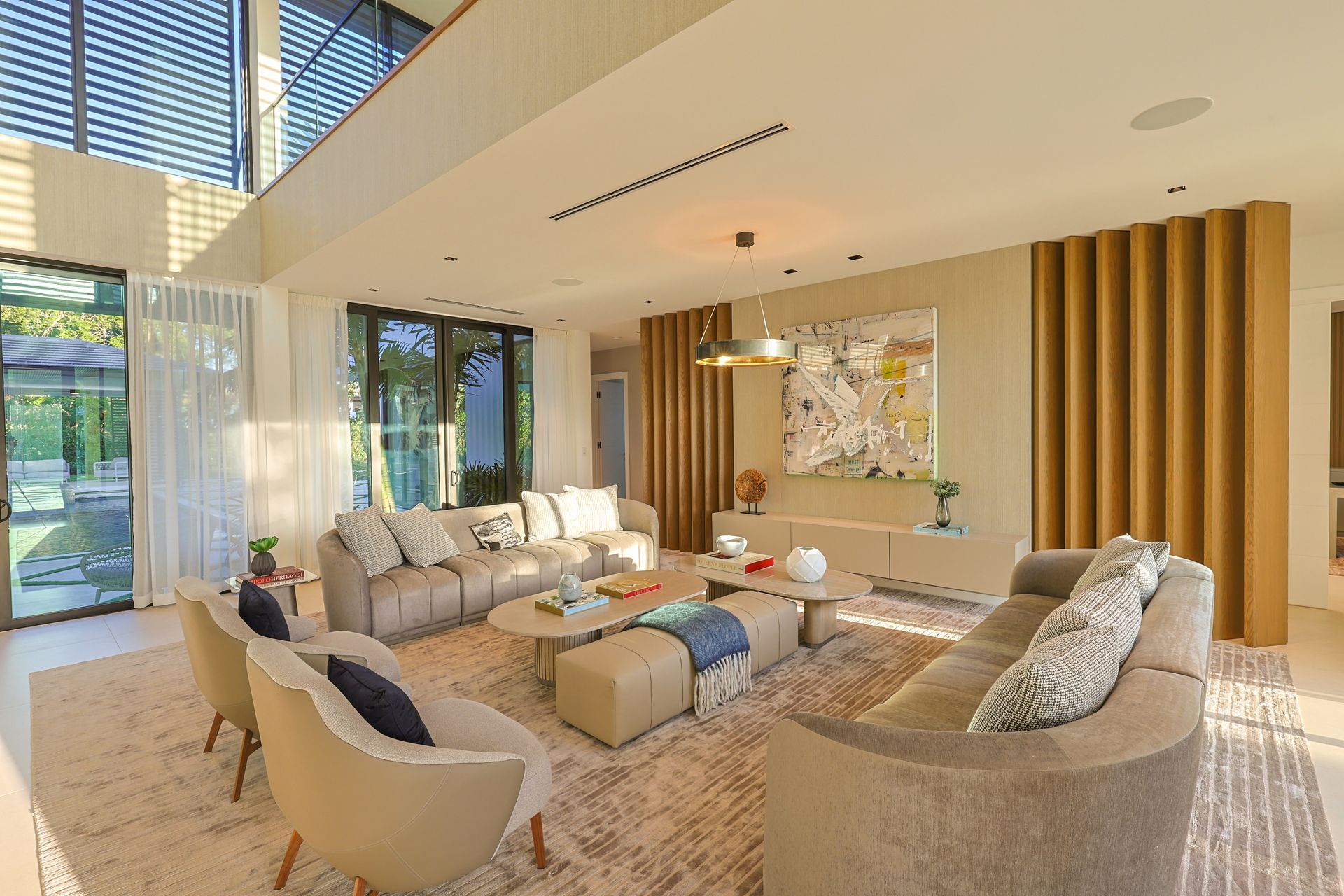Luxurious living room with beige sofas, wooden accents, and a large window overlooking a yard.