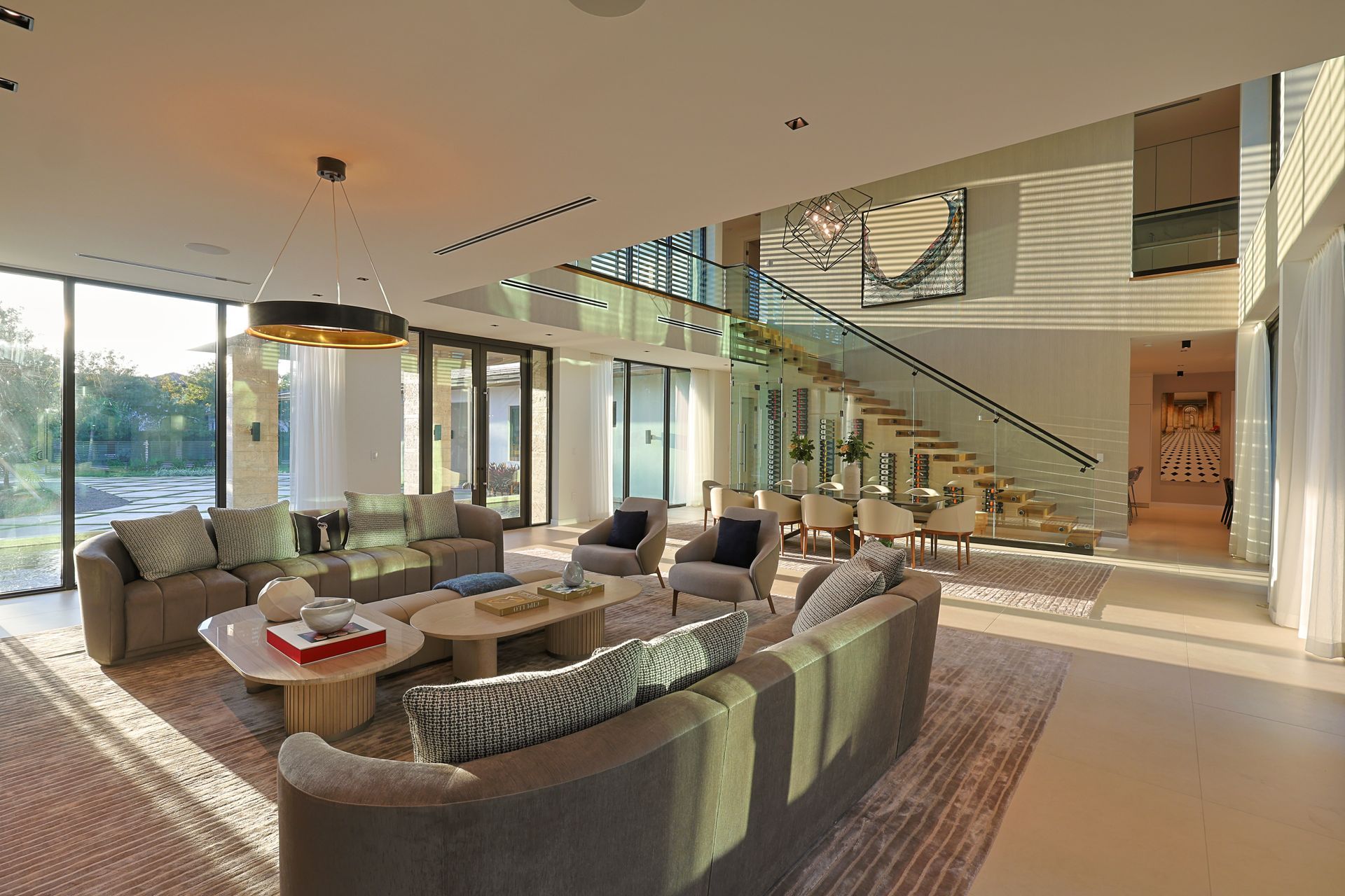 Spacious modern living room with large windows, neutral tones, and a floating staircase.