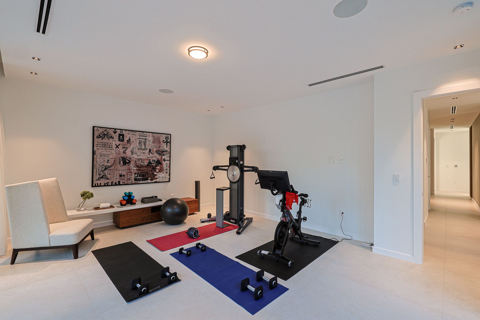 Home gym with exercise equipment: weights, mats, stationary bike, and a multi-station weight machine.