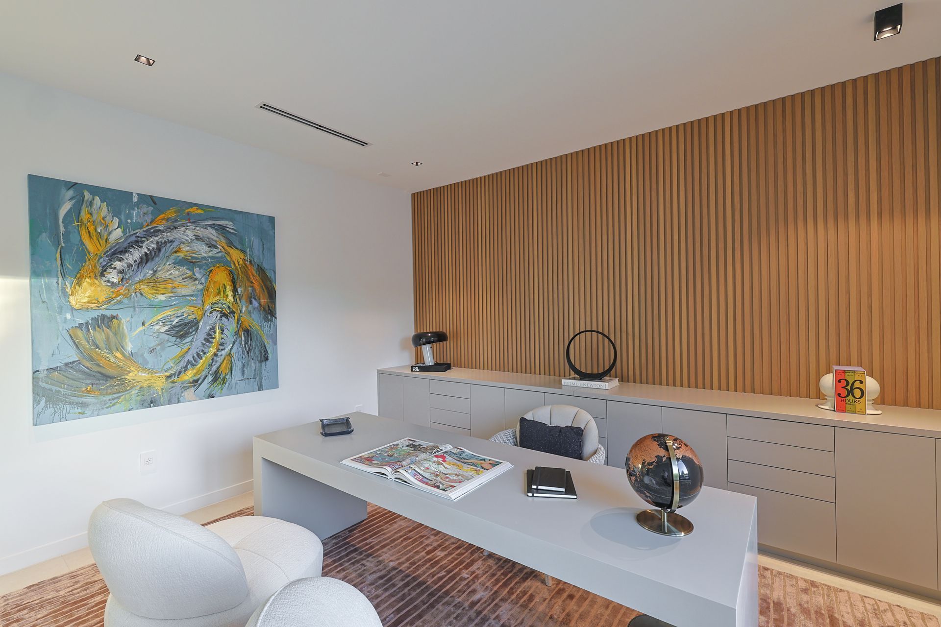 Modern office with light-gray desk, art, and tan wood paneling. A globe, books, and decor are displayed.