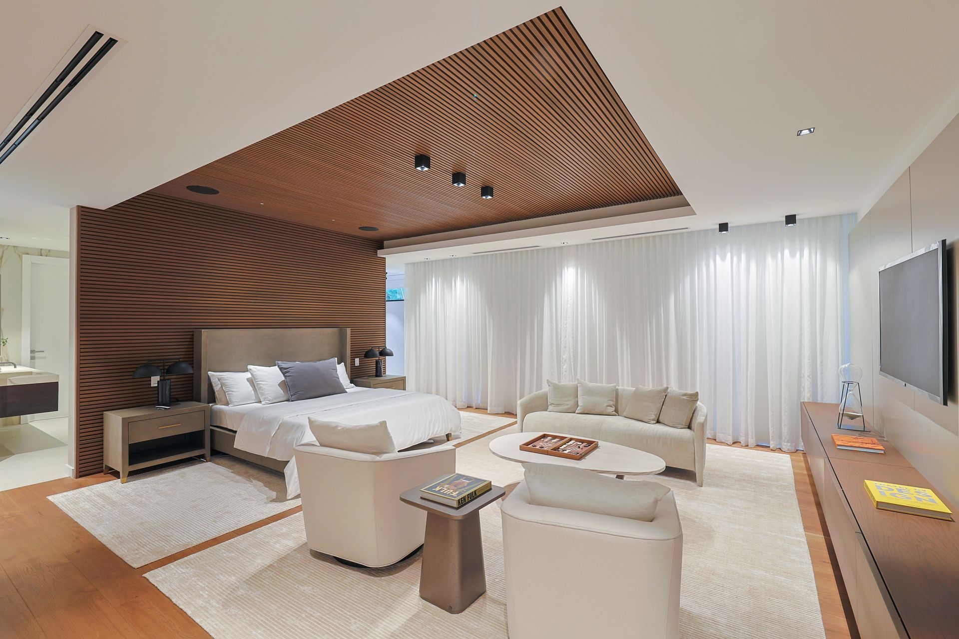 Luxurious bedroom with wood paneling, white curtains, bed, and seating area.
