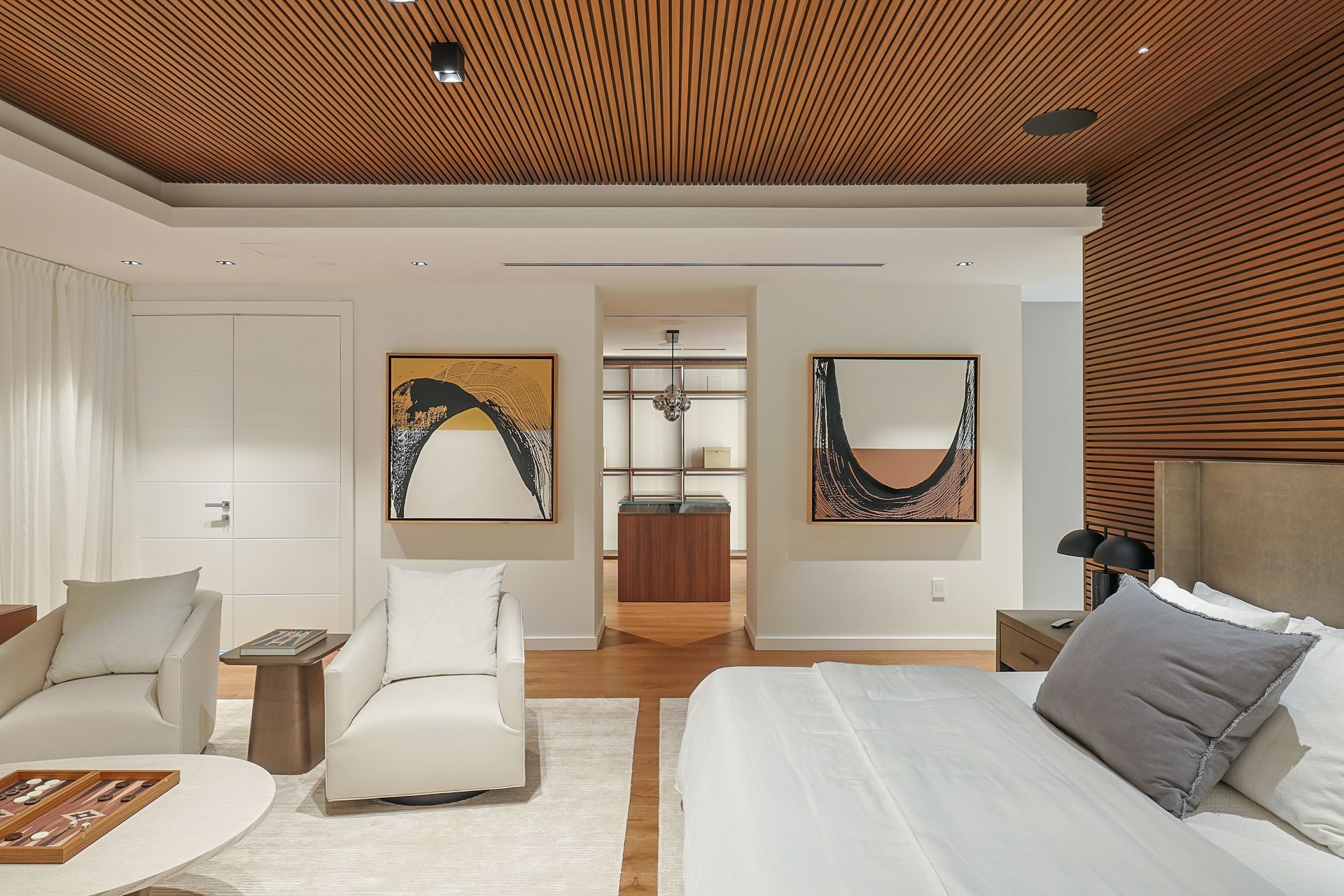 Bedroom interior with wood panel ceiling and walls, white furniture, artwork, and a walk-in closet.