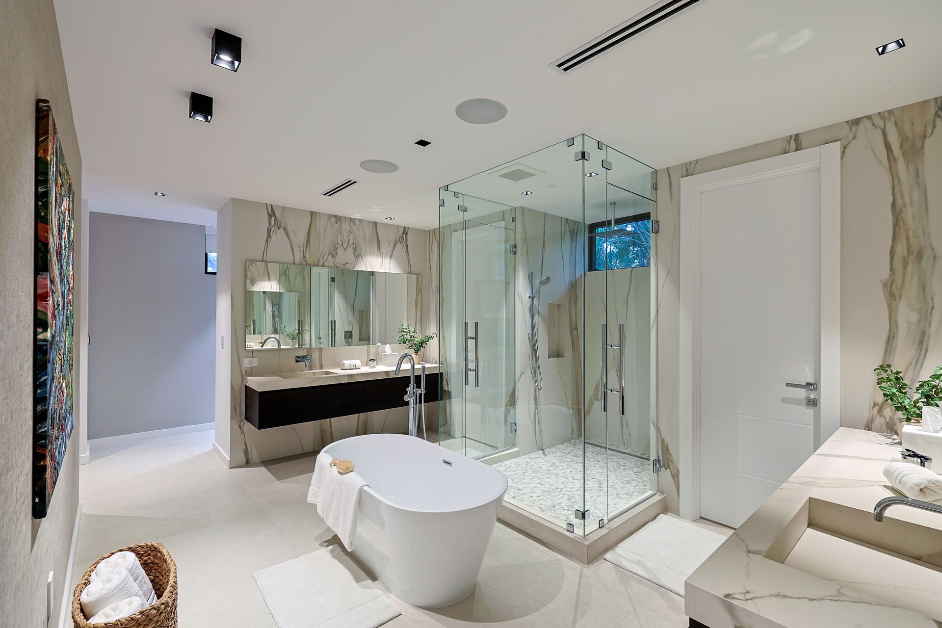Modern bathroom with marble walls, glass shower, freestanding tub, and double sinks.