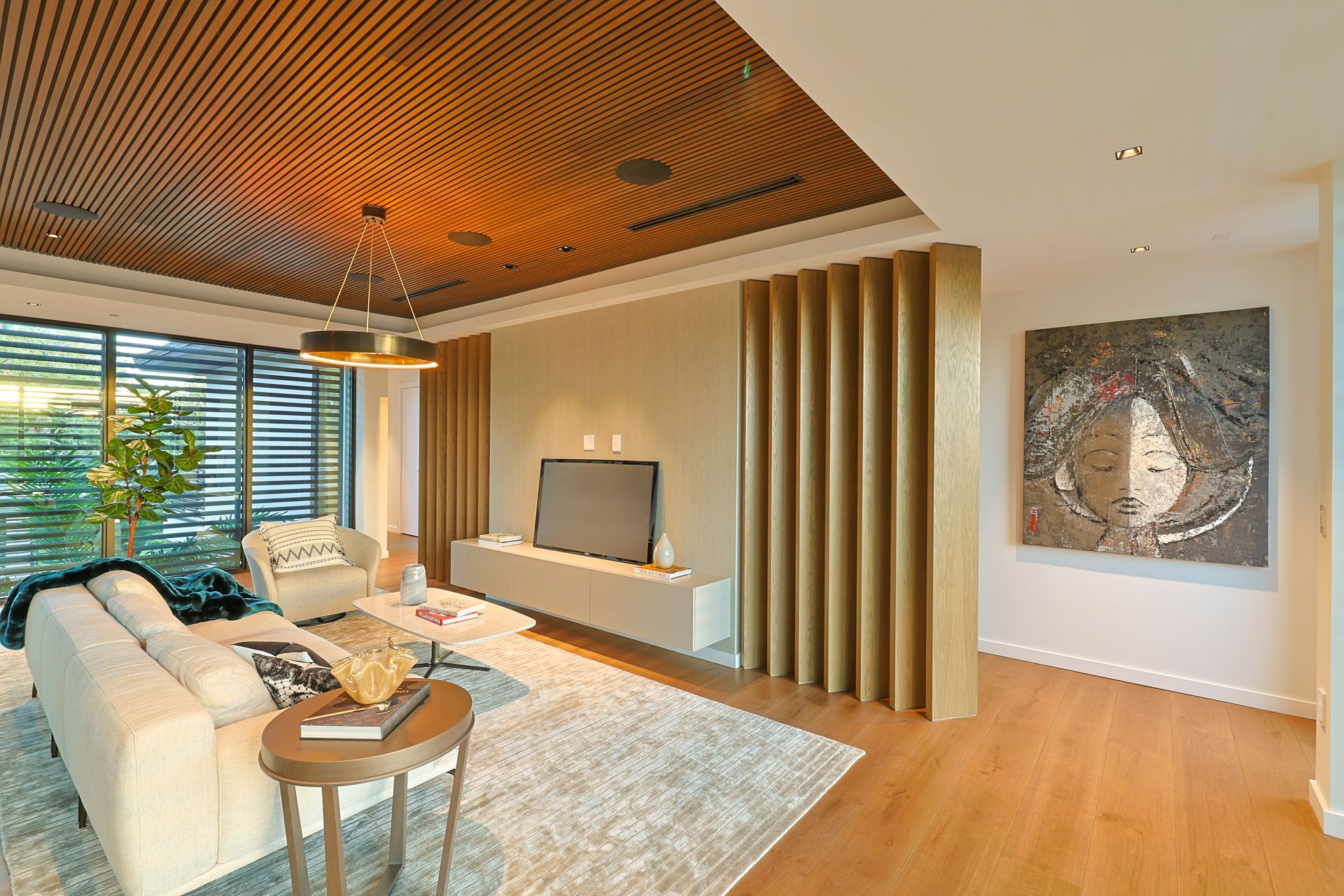 Living room with beige sofa, modern art, and a wood-paneled ceiling with an abstract design.
