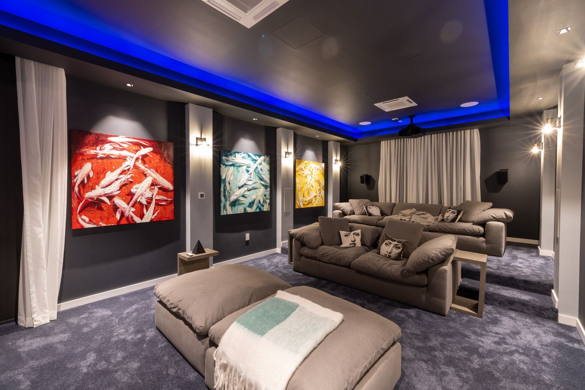 Home theater with tiered seating, blue carpet, art, and blue ceiling lighting.
