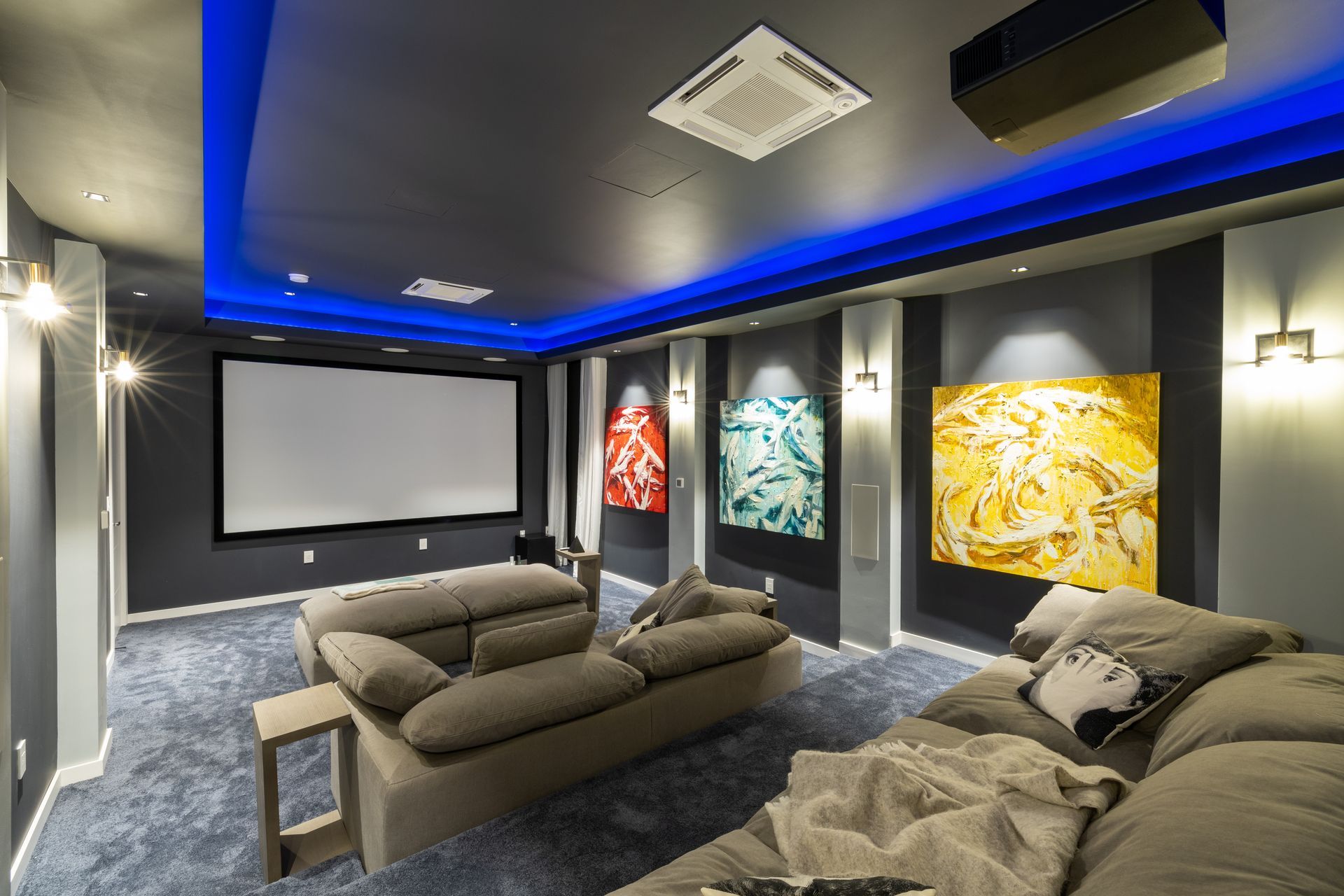 Home theater room with a large screen, blue lighting, and gray couches.