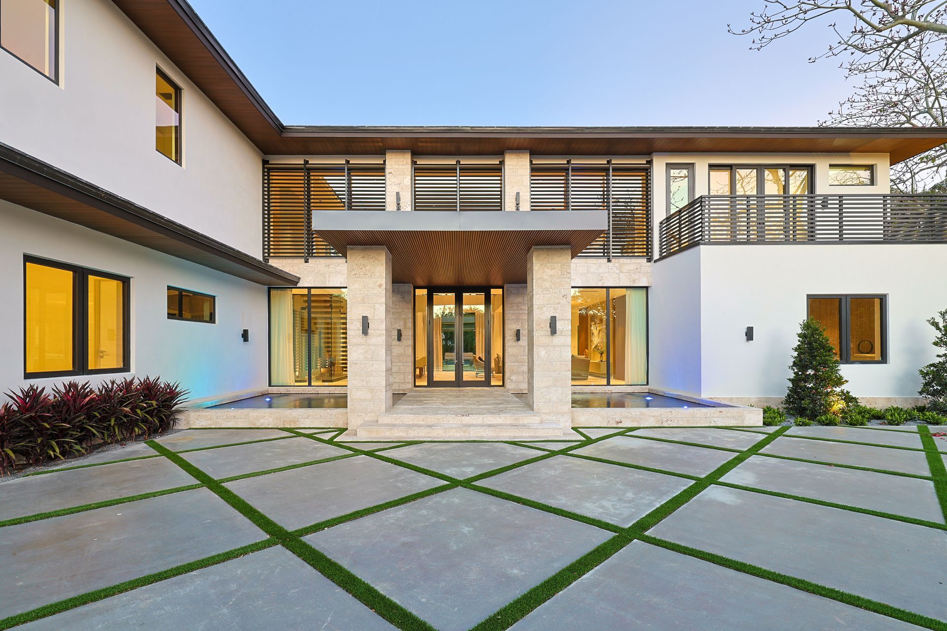 Modern white home with concrete driveway featuring green grass, glass doors, and decorative entry.