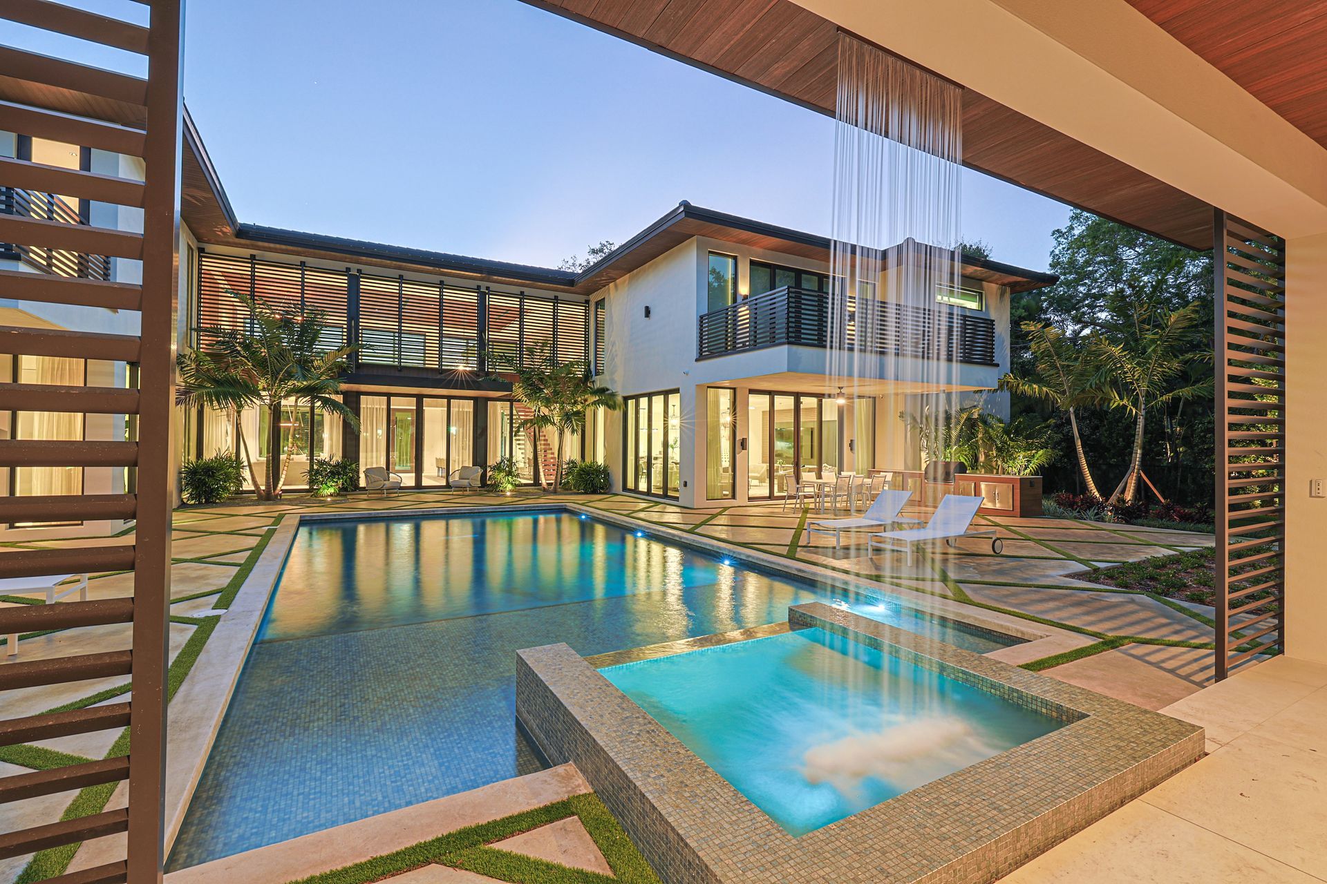 Modern house with a pool and waterfall; glass doors, stone patio, and manicured landscaping.