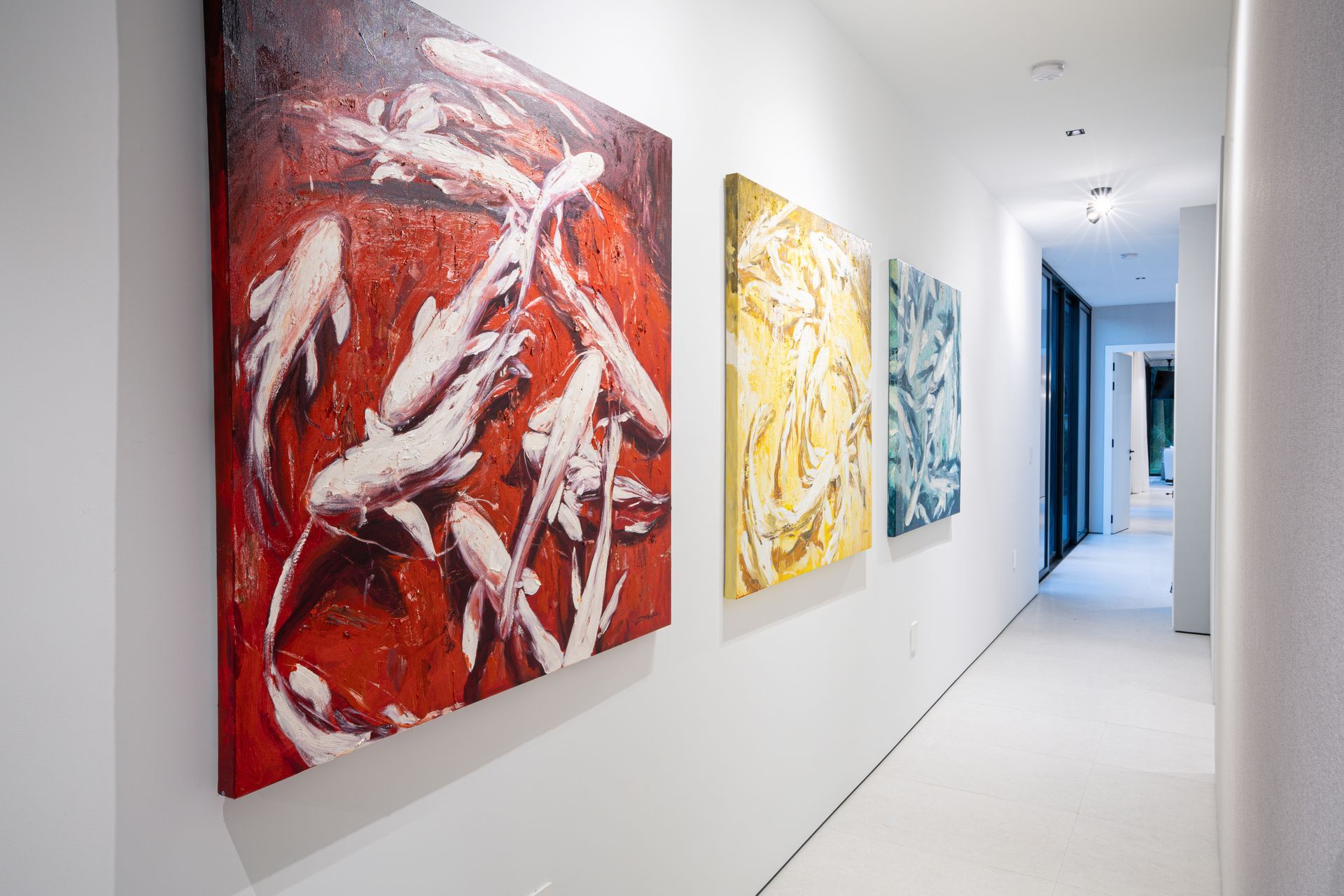 Long hallway with three colorful abstract paintings on white walls.
