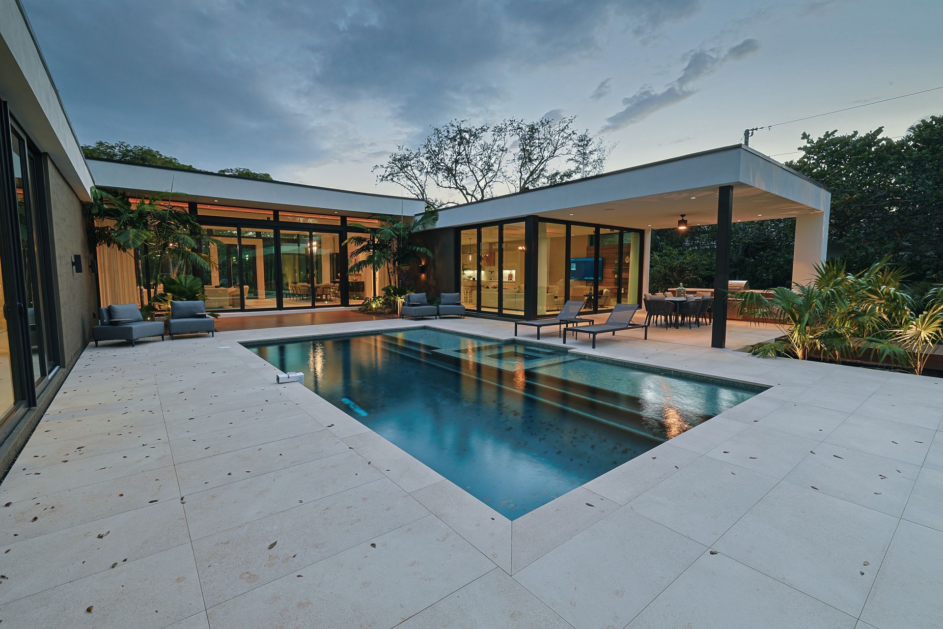 Modern home exterior with pool, patio, and outdoor dining area at dusk.