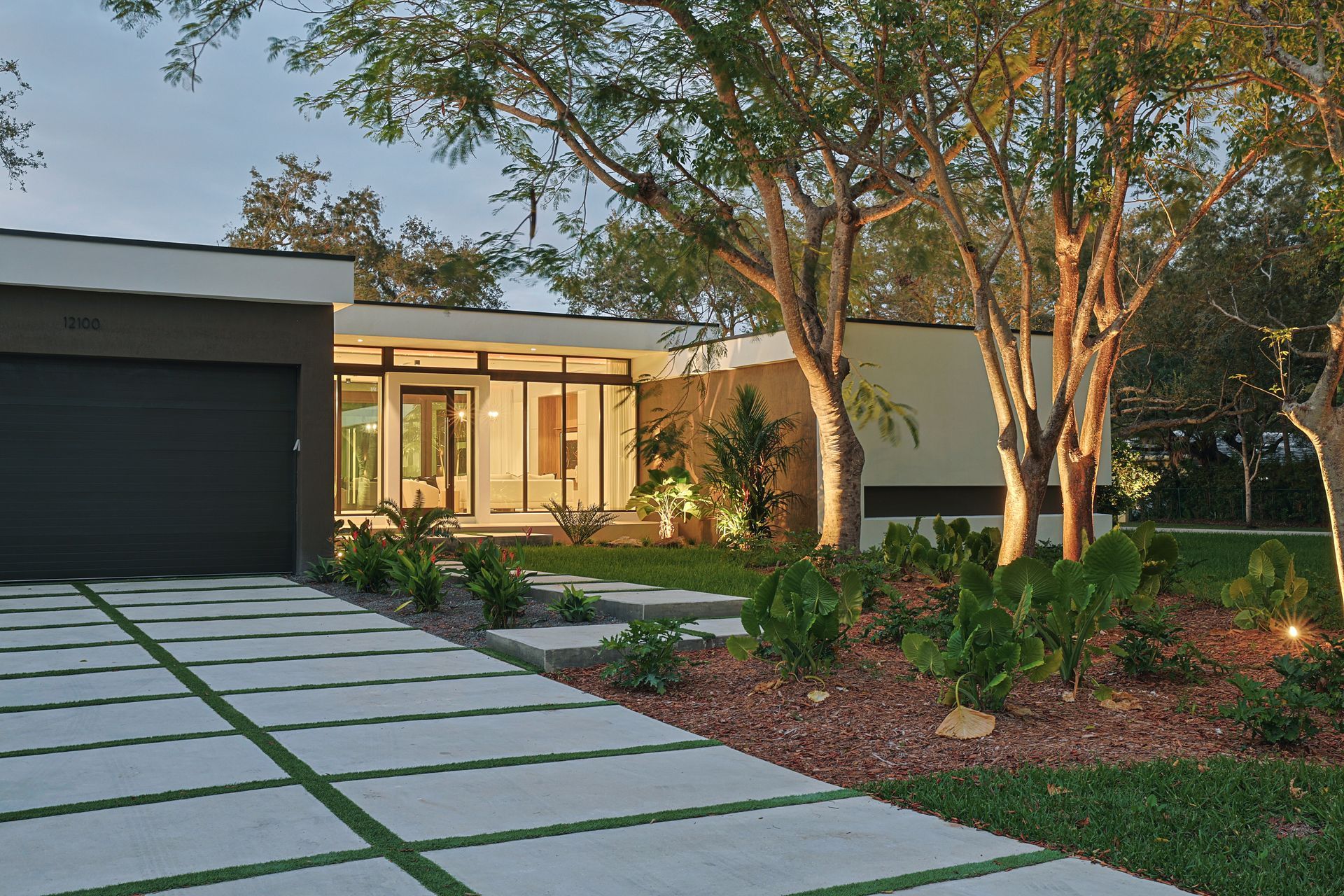 Modern house exterior with a driveway, landscaping, and trees.