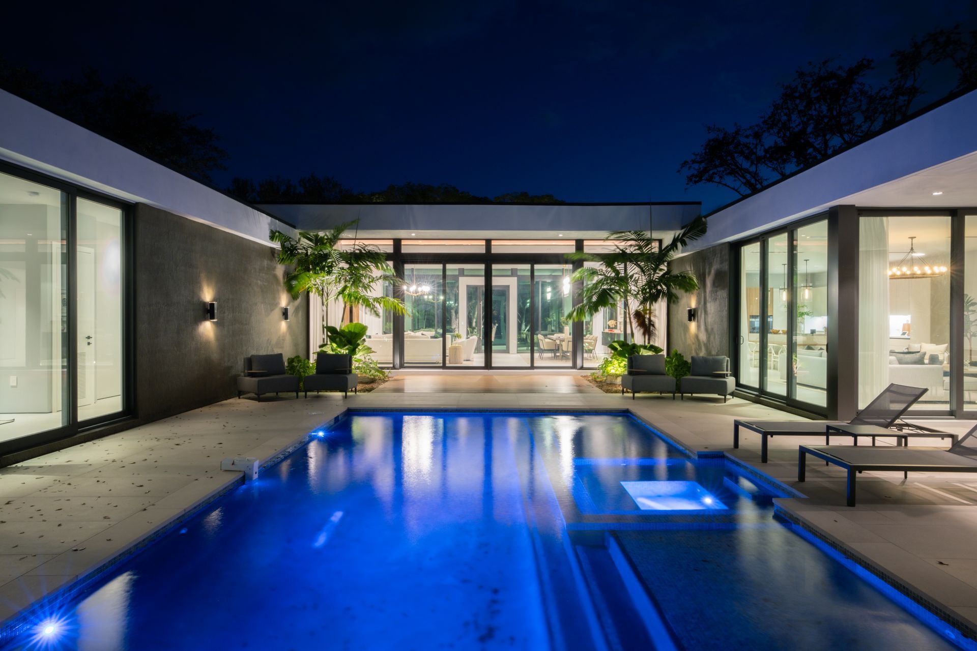 Night view of a modern home with a blue-lit pool and glass walls.