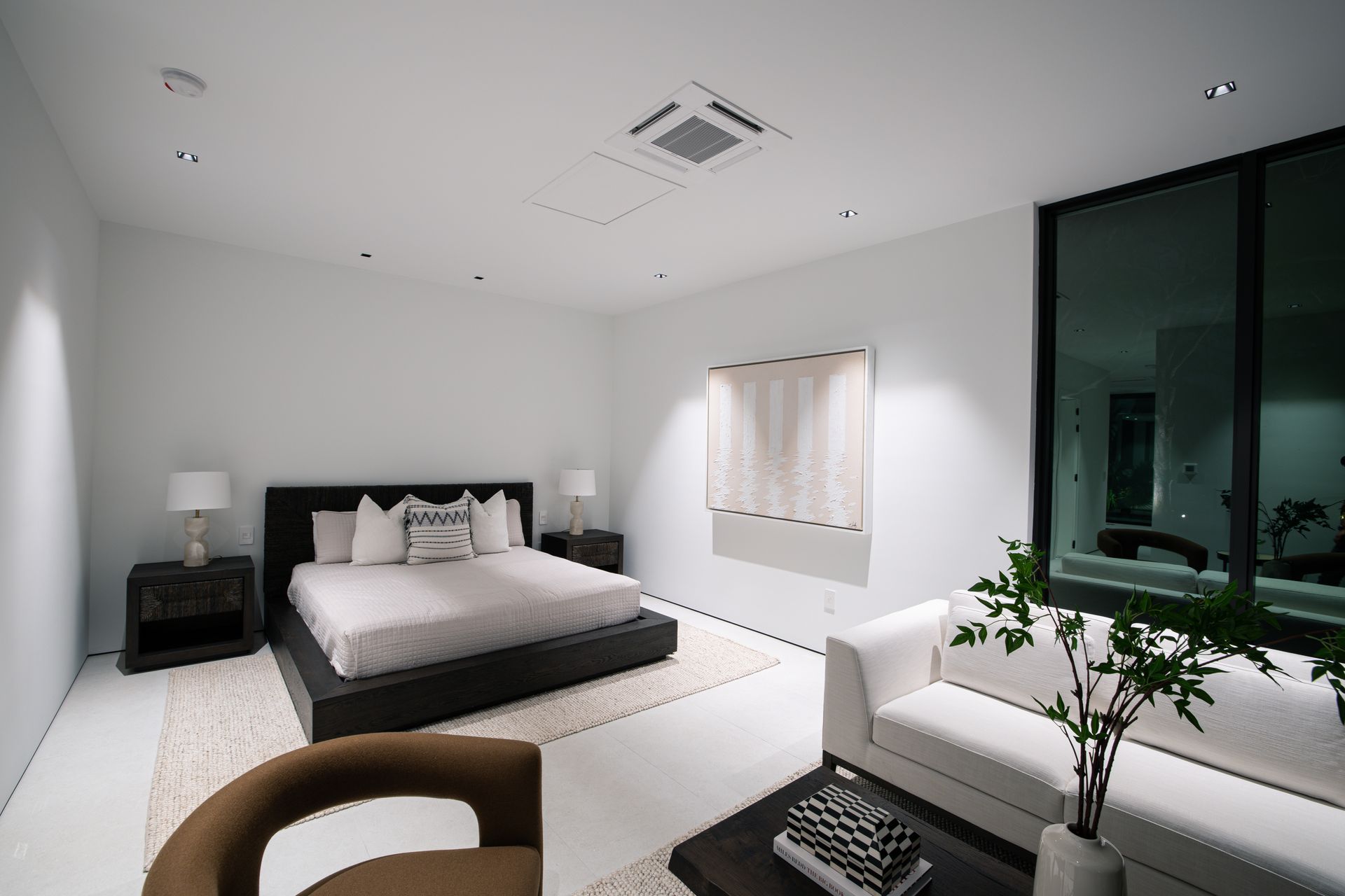 Modern white bedroom with a bed, sofa, and large window.
