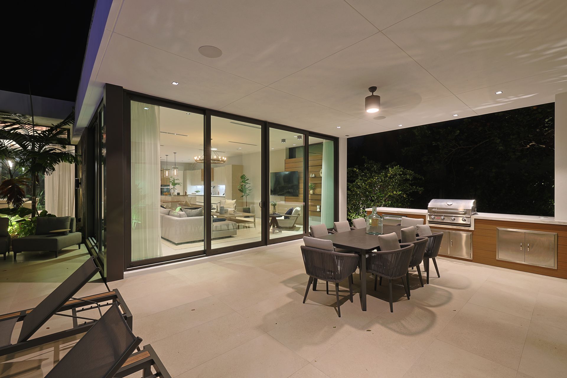 Patio with outdoor dining set and grill next to home with sliding glass doors and indoor living area.
