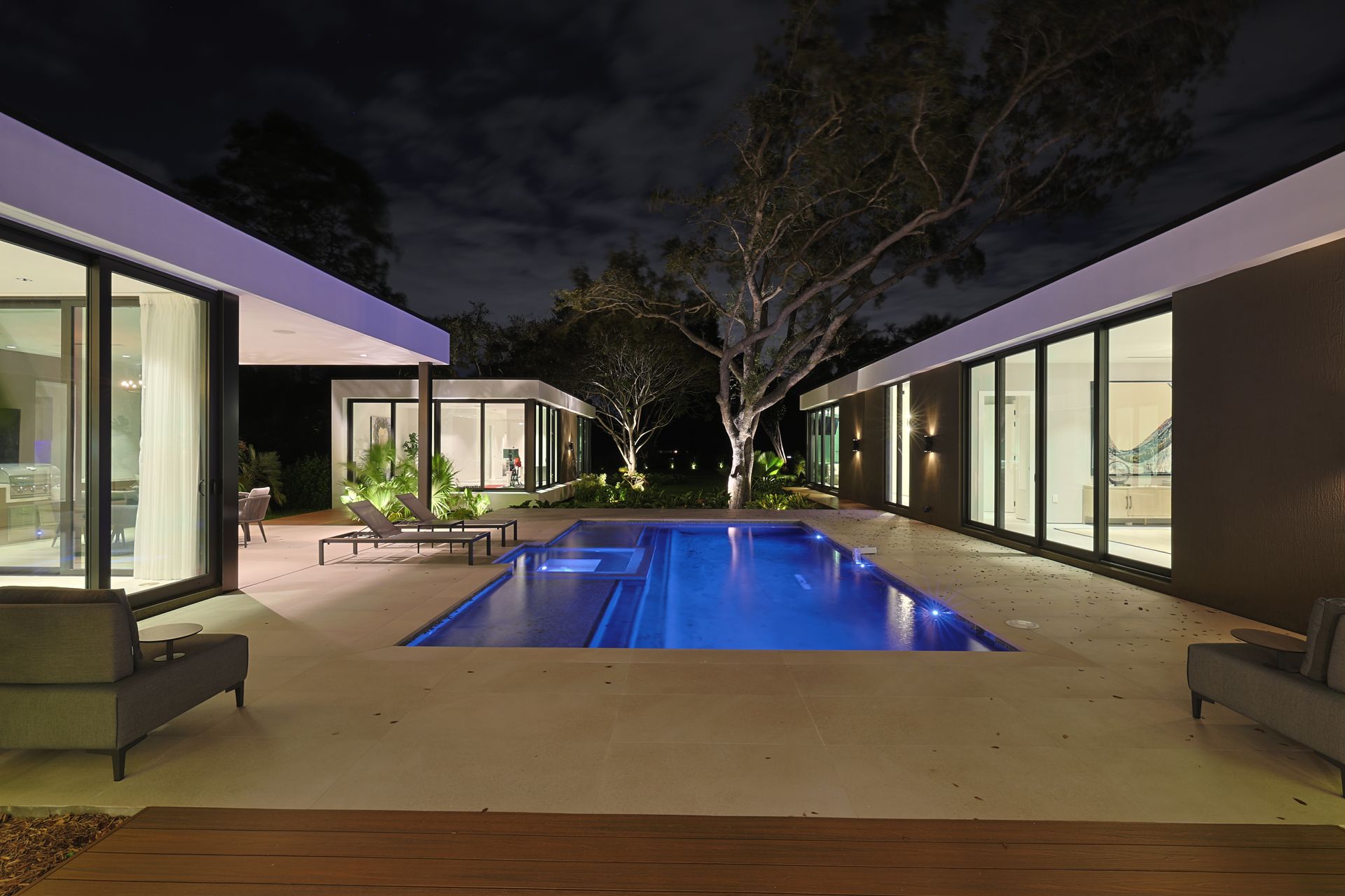 Nighttime view of modern homes flanking a blue-lit pool.