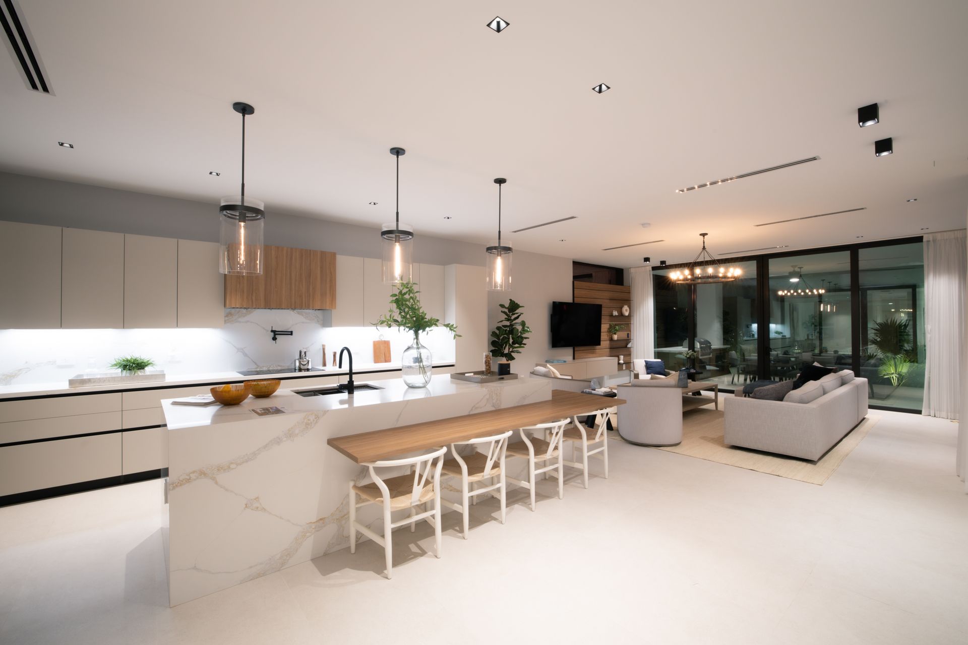 Modern open-plan kitchen and living room with white and wood accents, island with seating, and large windows.