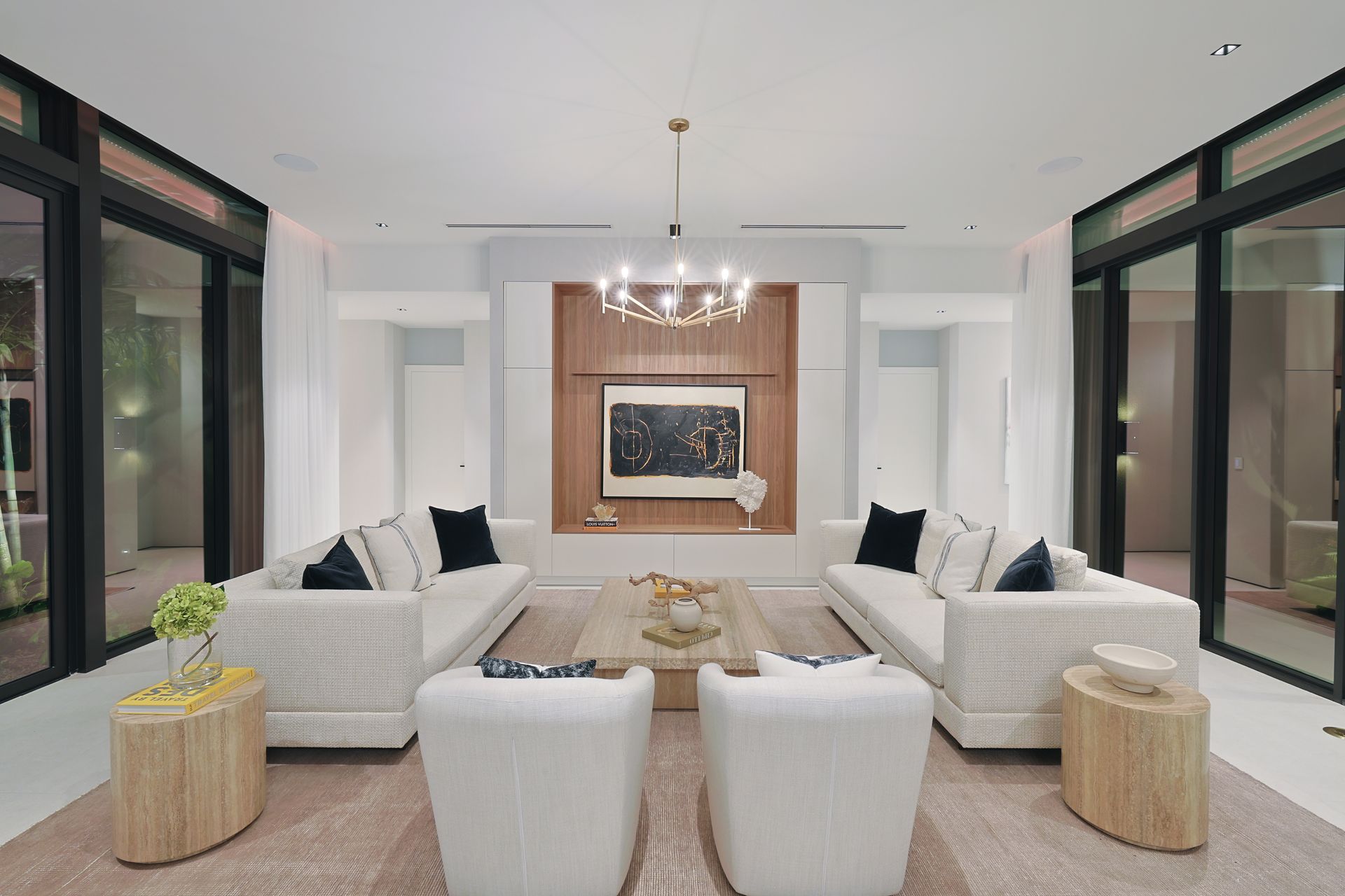 Modern living room with white sofas, chairs, and a central coffee table, accented by black window frames and wooden panels.