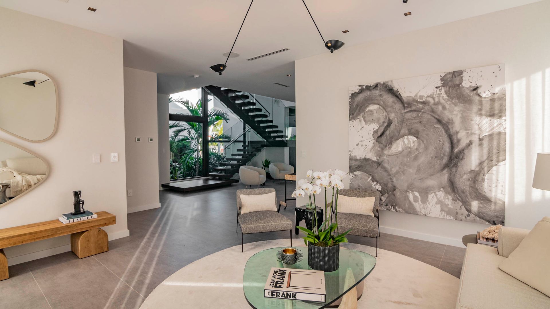 Modern living room with artwork, staircase, and glass coffee table.