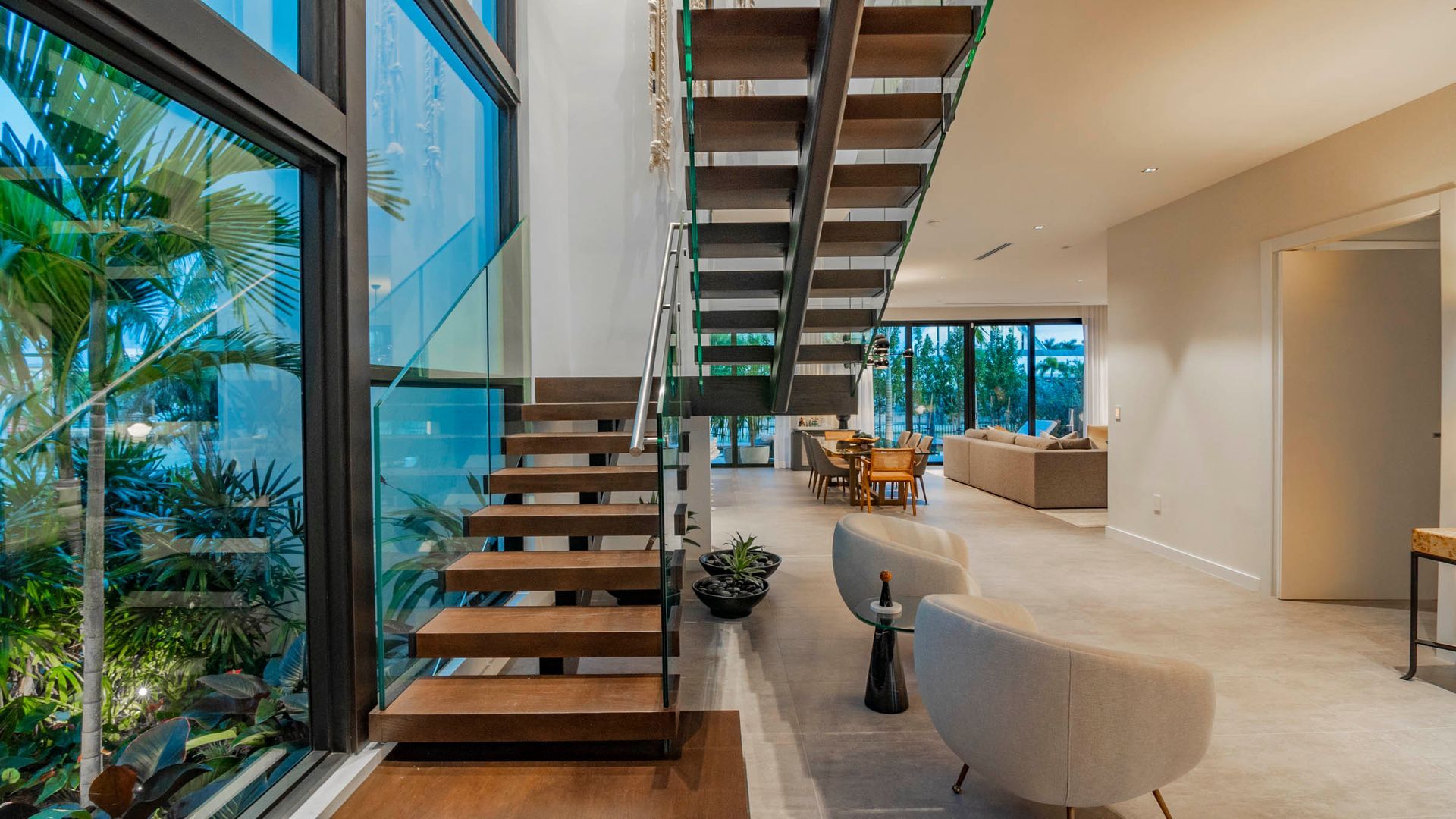 Modern home interior with wooden staircase, glass walls, and open living area.