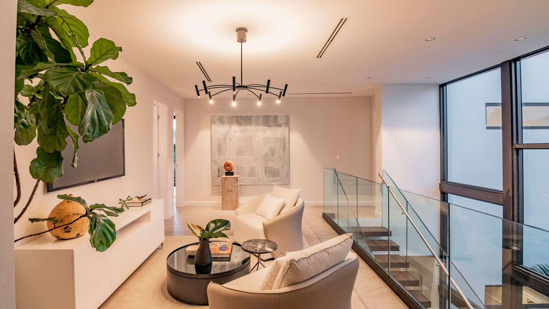 Modern living room with neutral colors, glass railing, and art.
