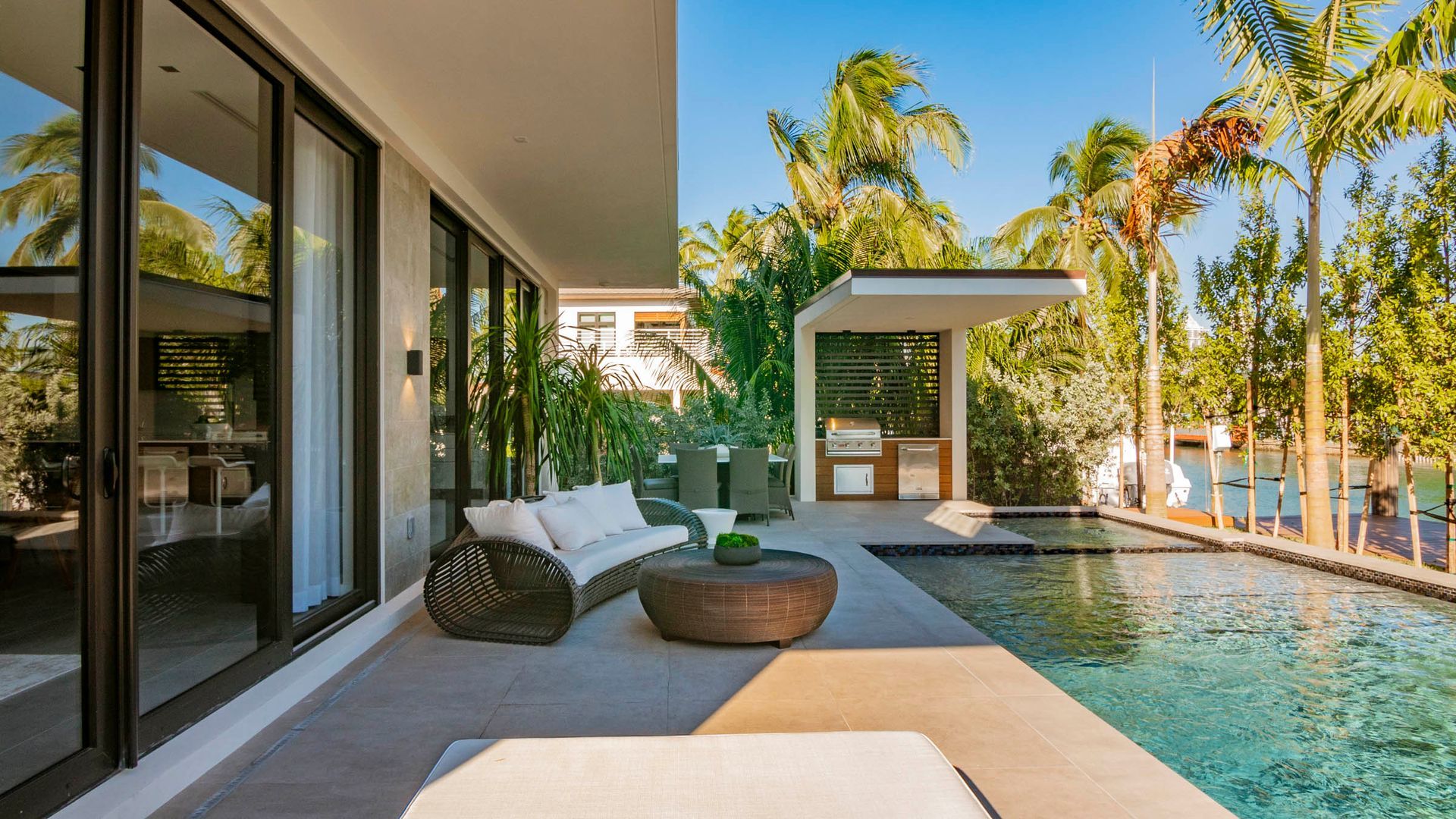 Patio with outdoor seating next to a pool under a clear blue sky.