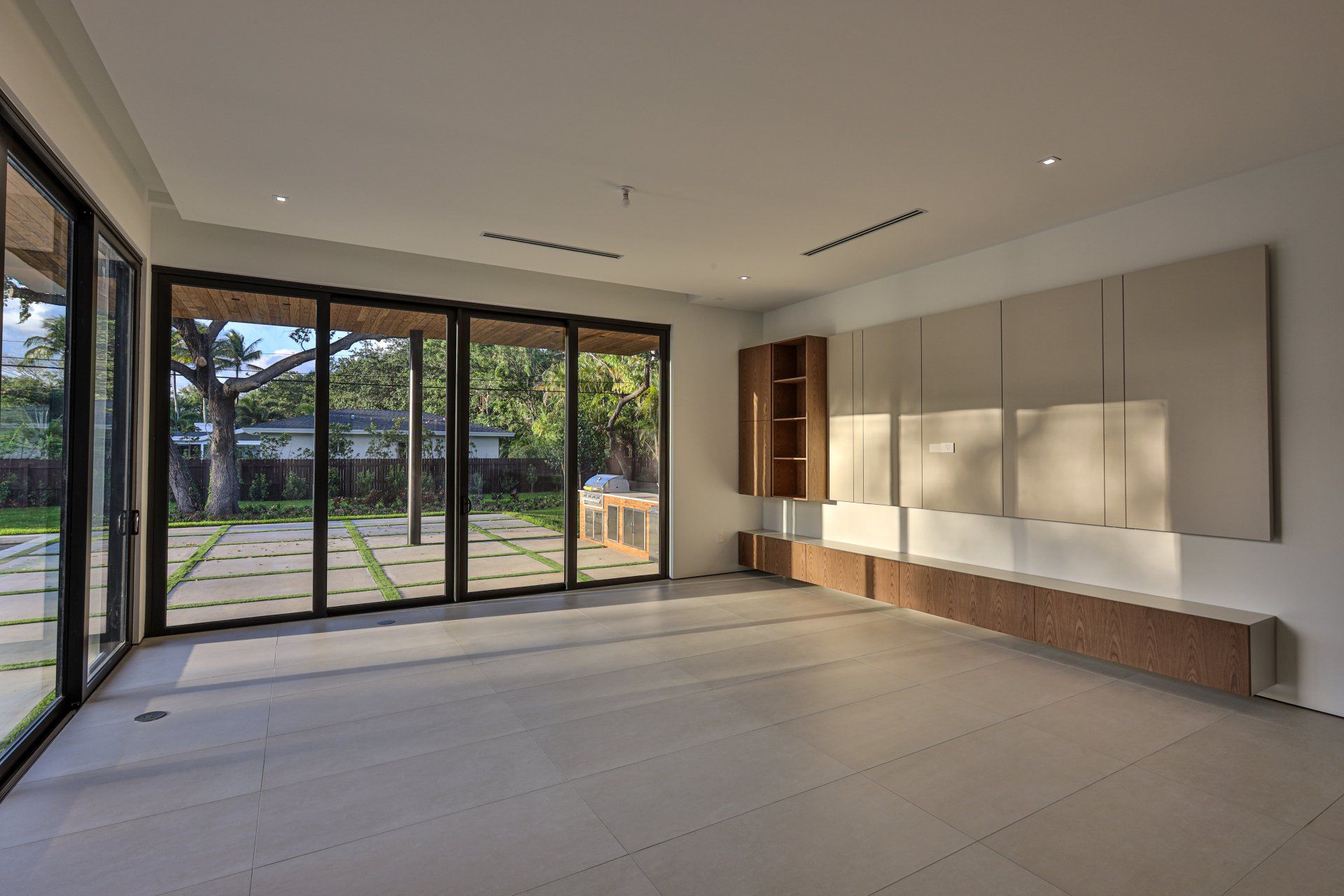 Empty, modern room with large glass doors overlooking a backyard. Built-in cabinetry on wall and floor.