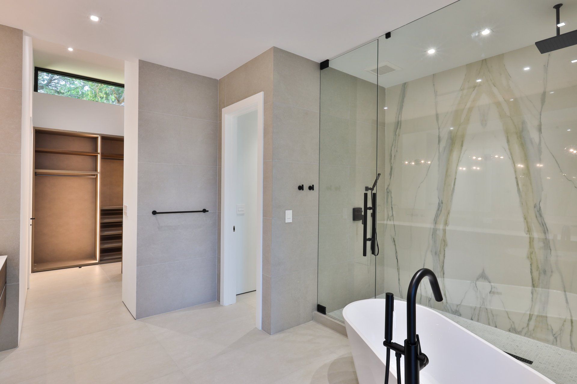 Modern bathroom with walk-in shower, freestanding tub, walk-in closet, neutral colors, black fixtures, and marble walls.