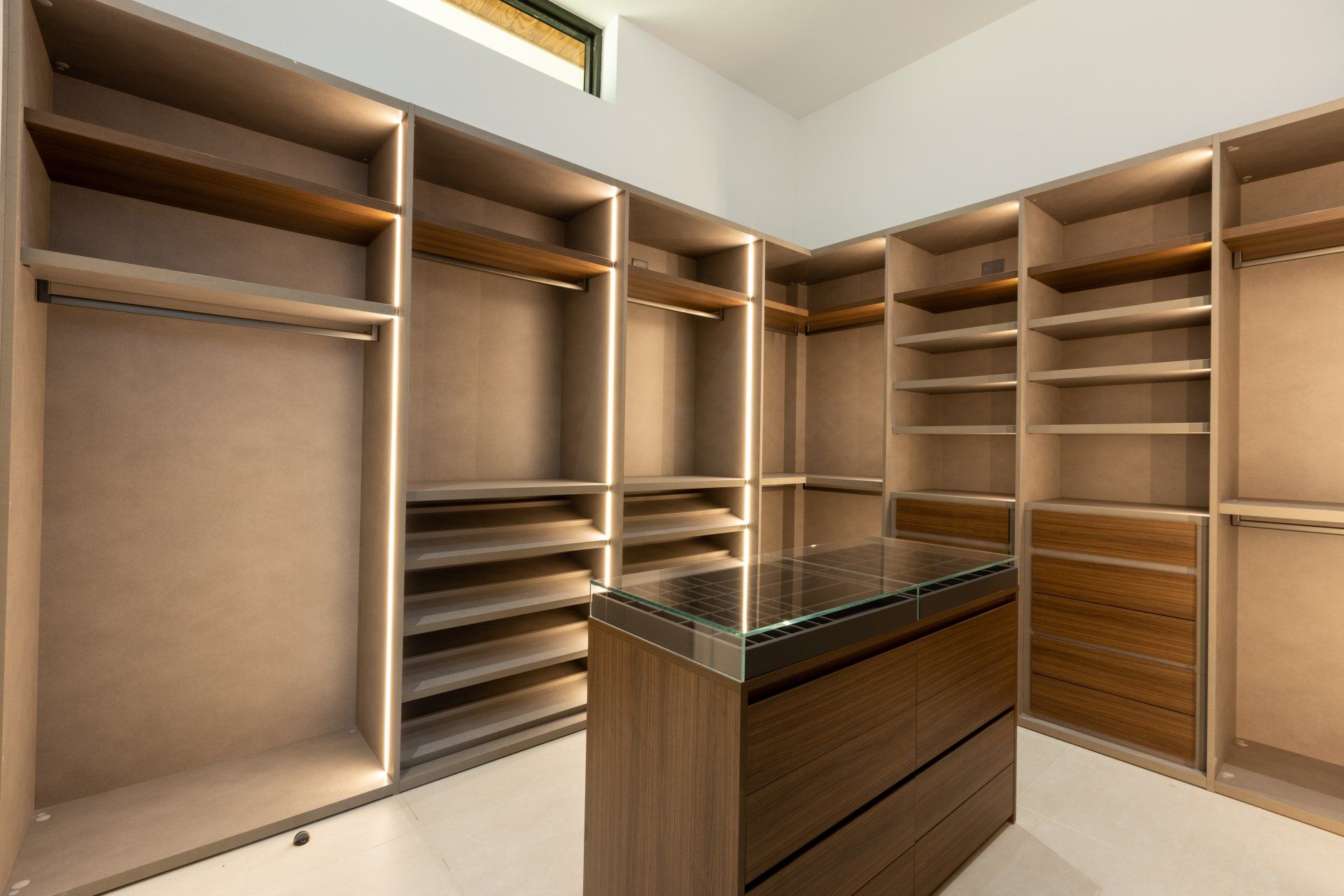 Walk-in closet with built-in shelves, hanging rods, and a center island, all in light wood with integrated lighting.