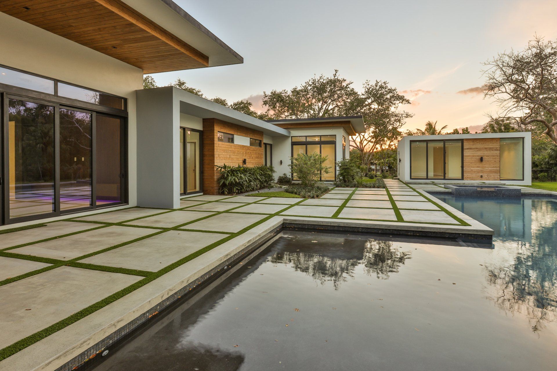 Modern home with pool and water feature, concrete pathway, and glass walls.