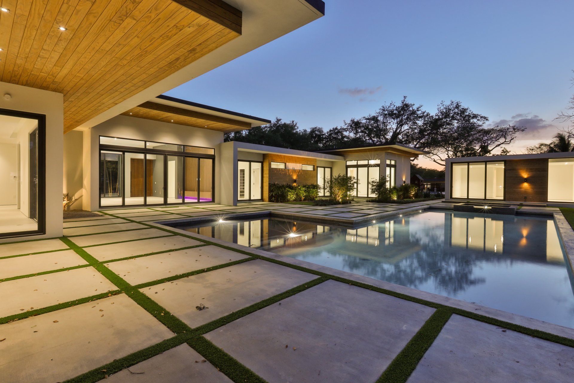 Modern luxury home with pool, reflecting evening sky; concrete patio with grass accents.