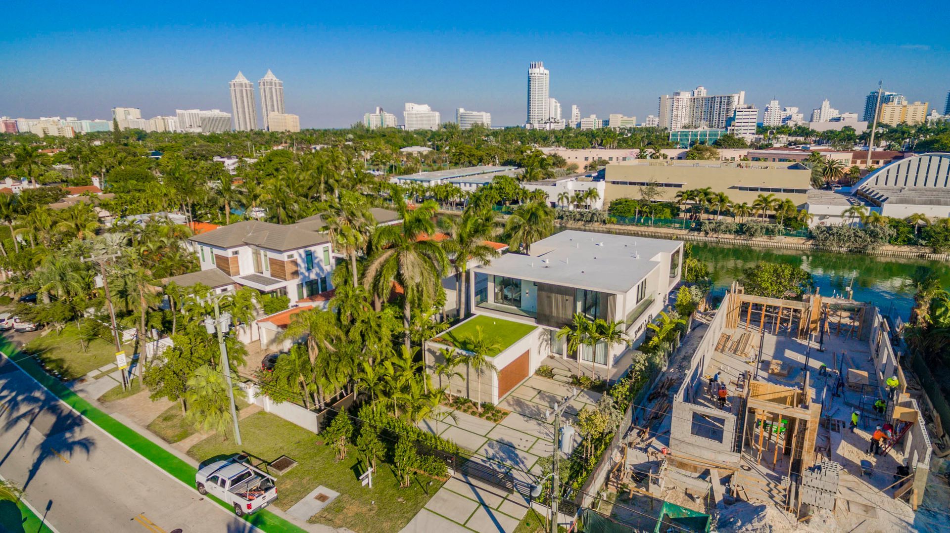 Aerial view of homes with lush trees and a city skyline in the background on a sunny day.