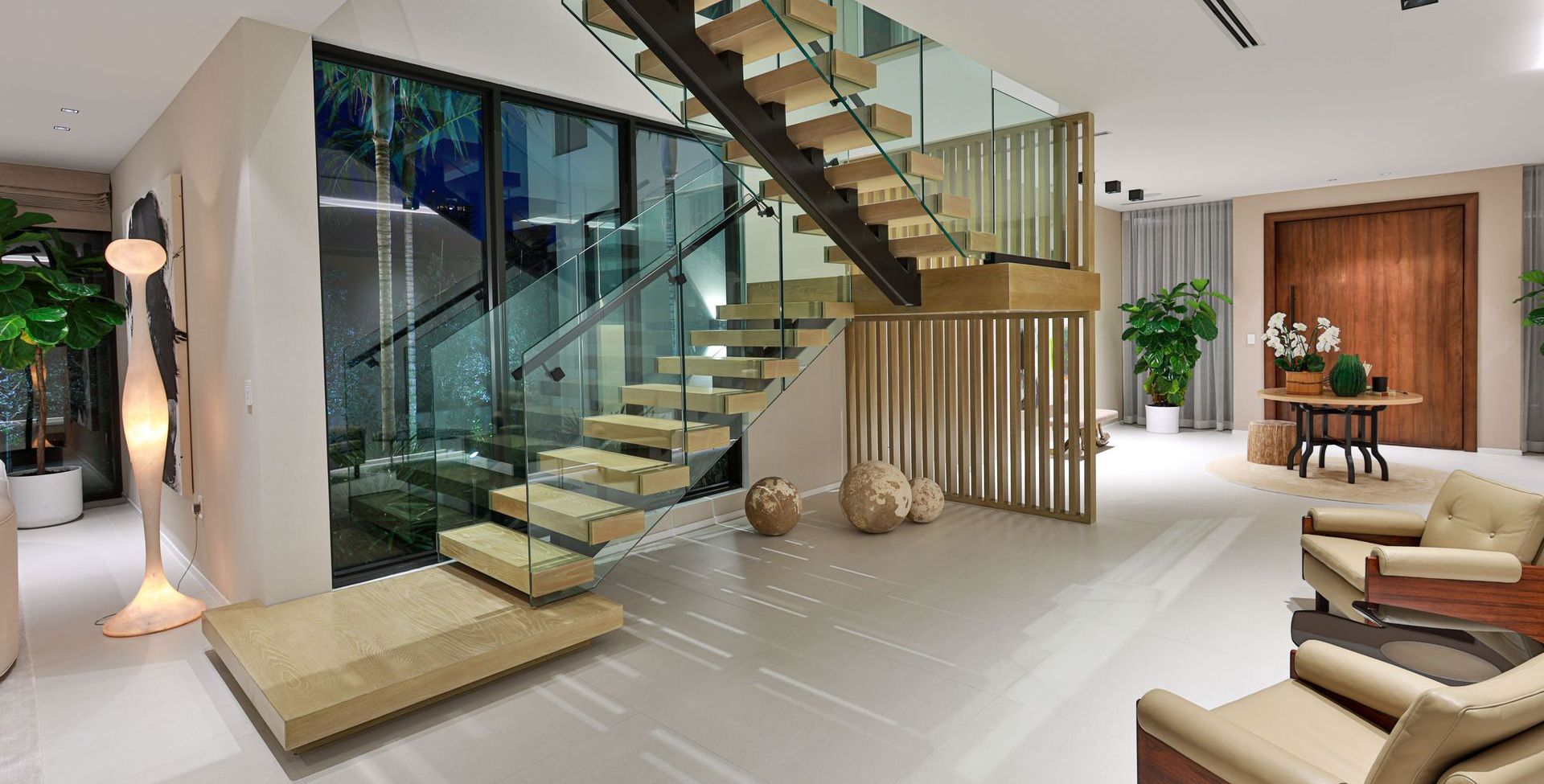 Modern interior with floating staircase, glass walls, and beige furniture.