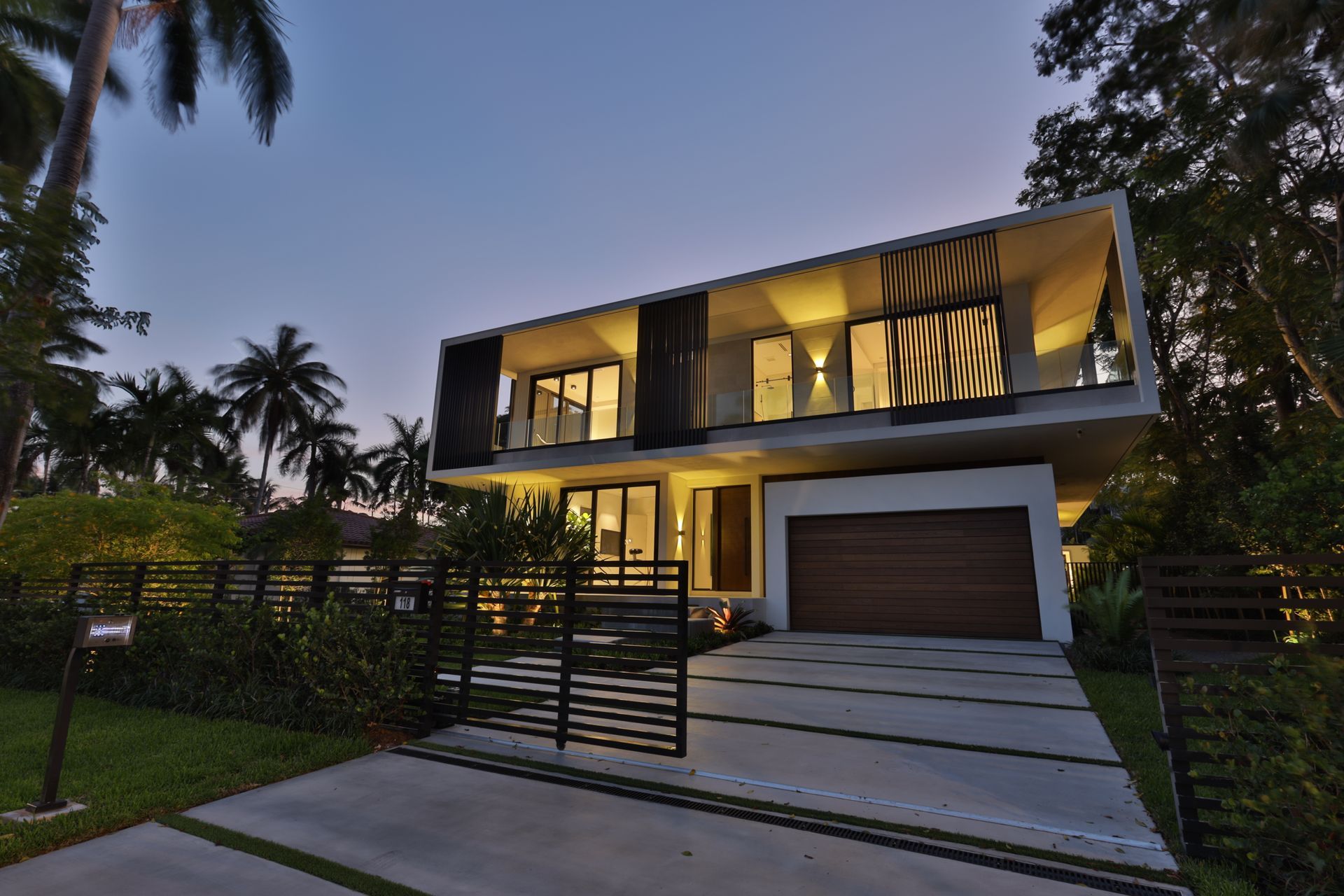Modern two-story house with a wooden garage door and a driveway, lit at dusk.