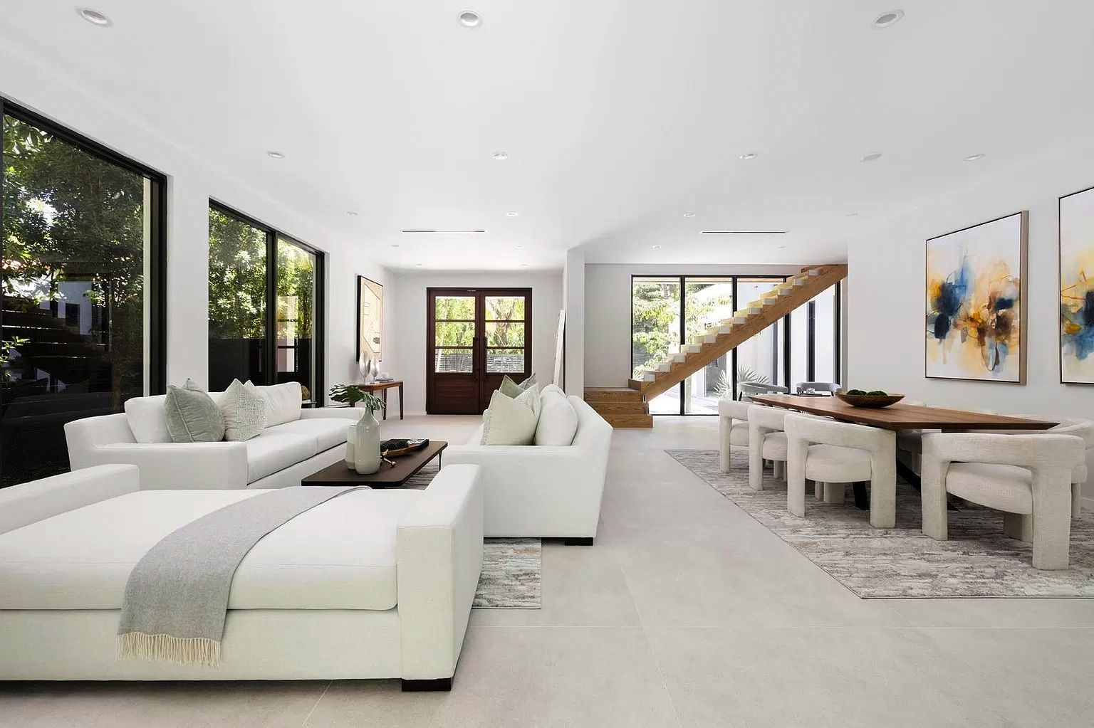 Bright, modern living space. White sofas, dining table, art, and large windows.