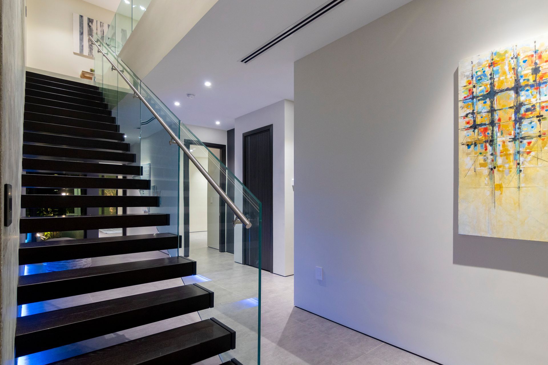 A staircase with a glass railing and a painting on the wall
