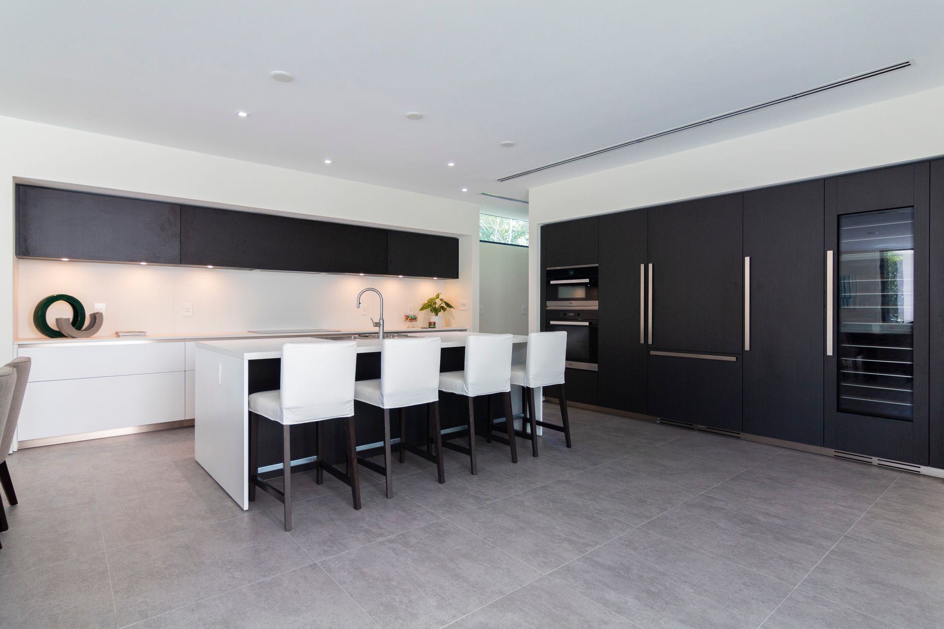A kitchen with black cabinets and white chairs