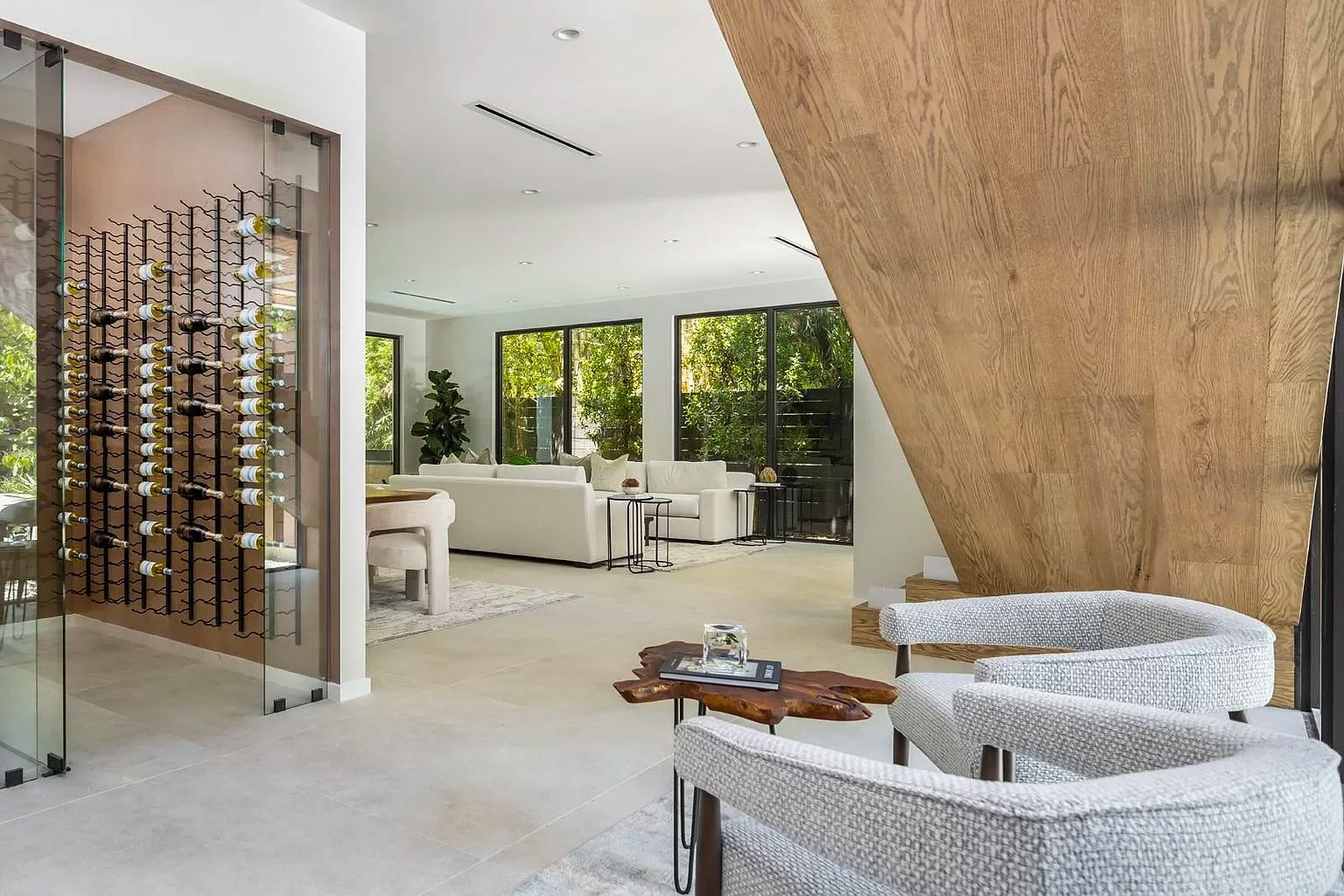 Modern living room with wine cellar, white furniture, and a natural wood accent wall.