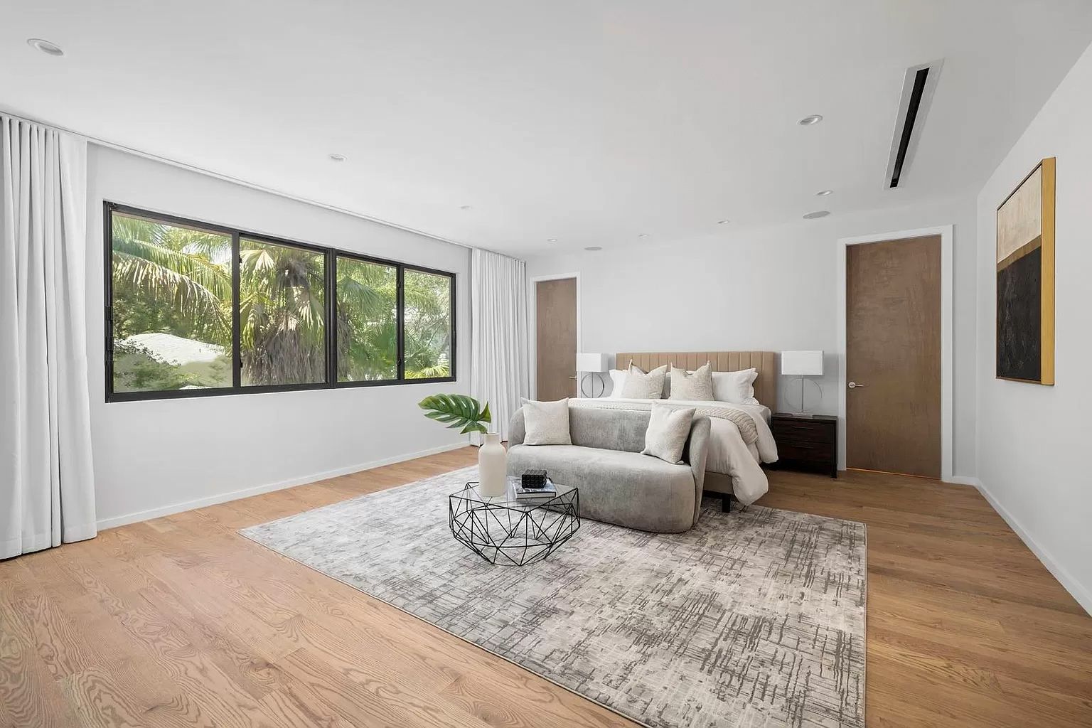 Spacious bedroom with large window, neutral colors, hardwood floors, a rug, and a sofa.