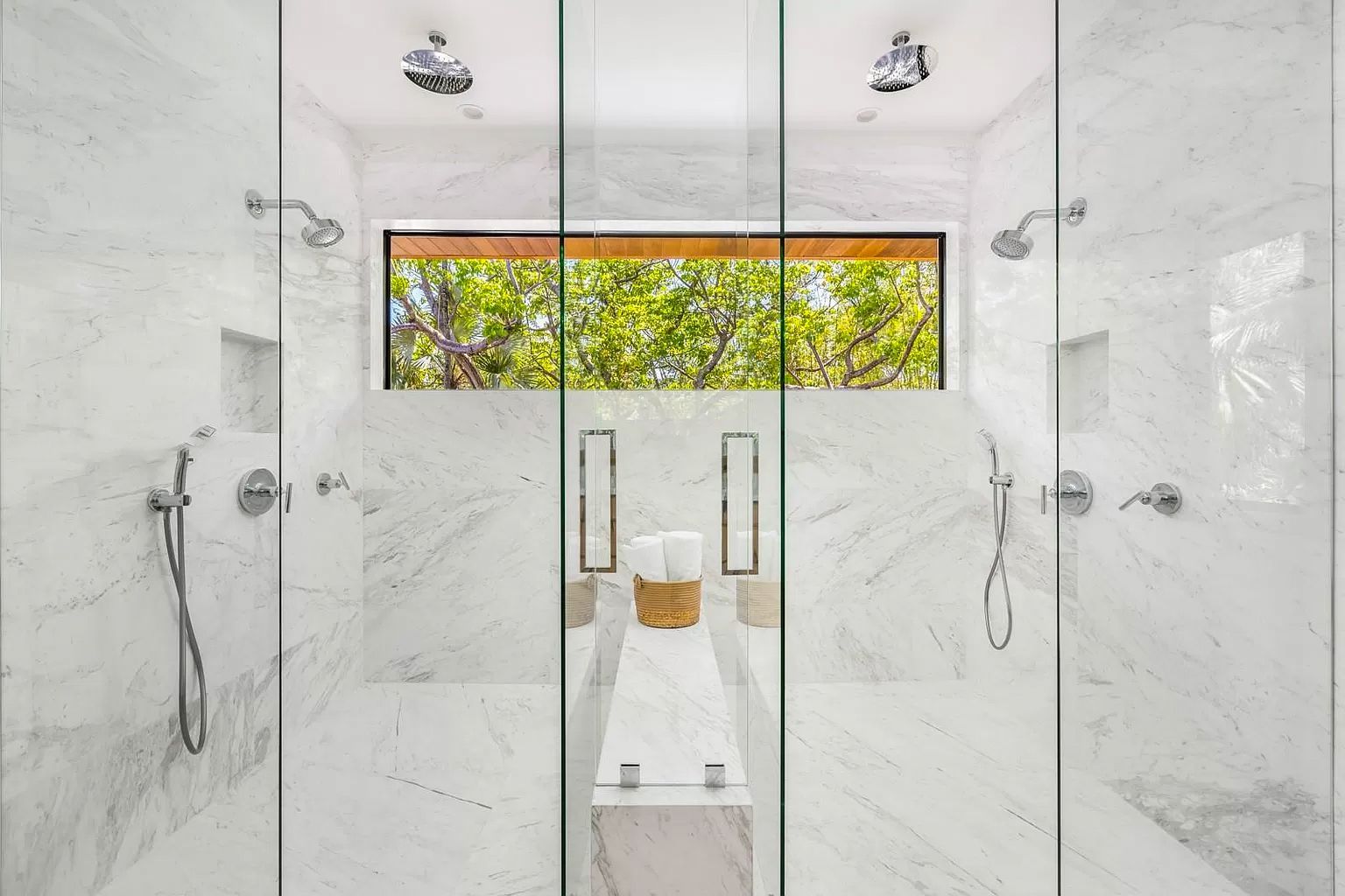 Spacious marble bathroom with three glass-enclosed shower stalls; a window overlooks trees.
