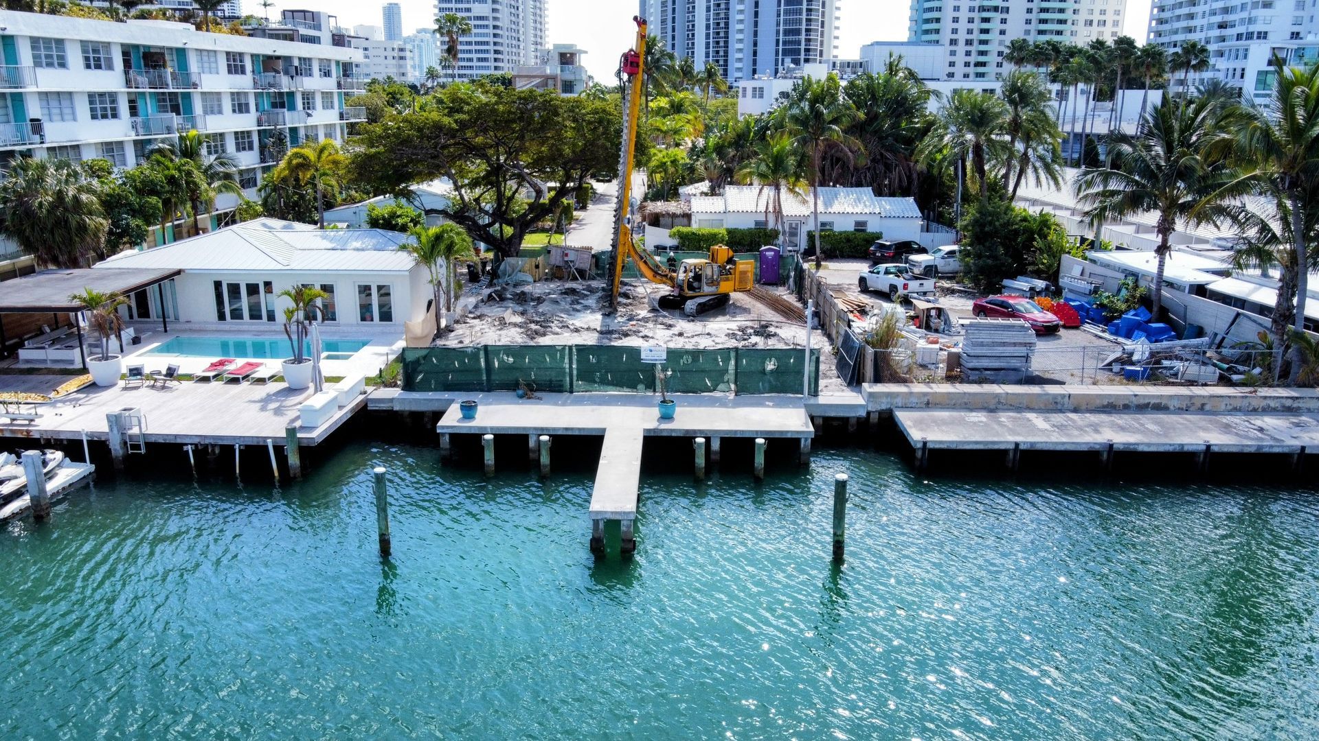 Construction site with waterfront docks and buildings; a yellow crane, water, and blue sky.