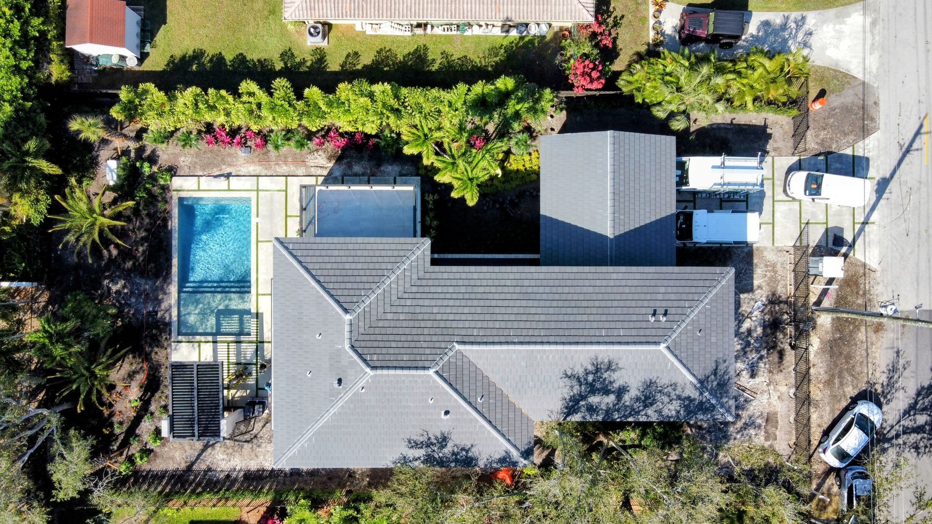 Overhead view of a house with a pool, green lawn, and vehicles parked on the street.